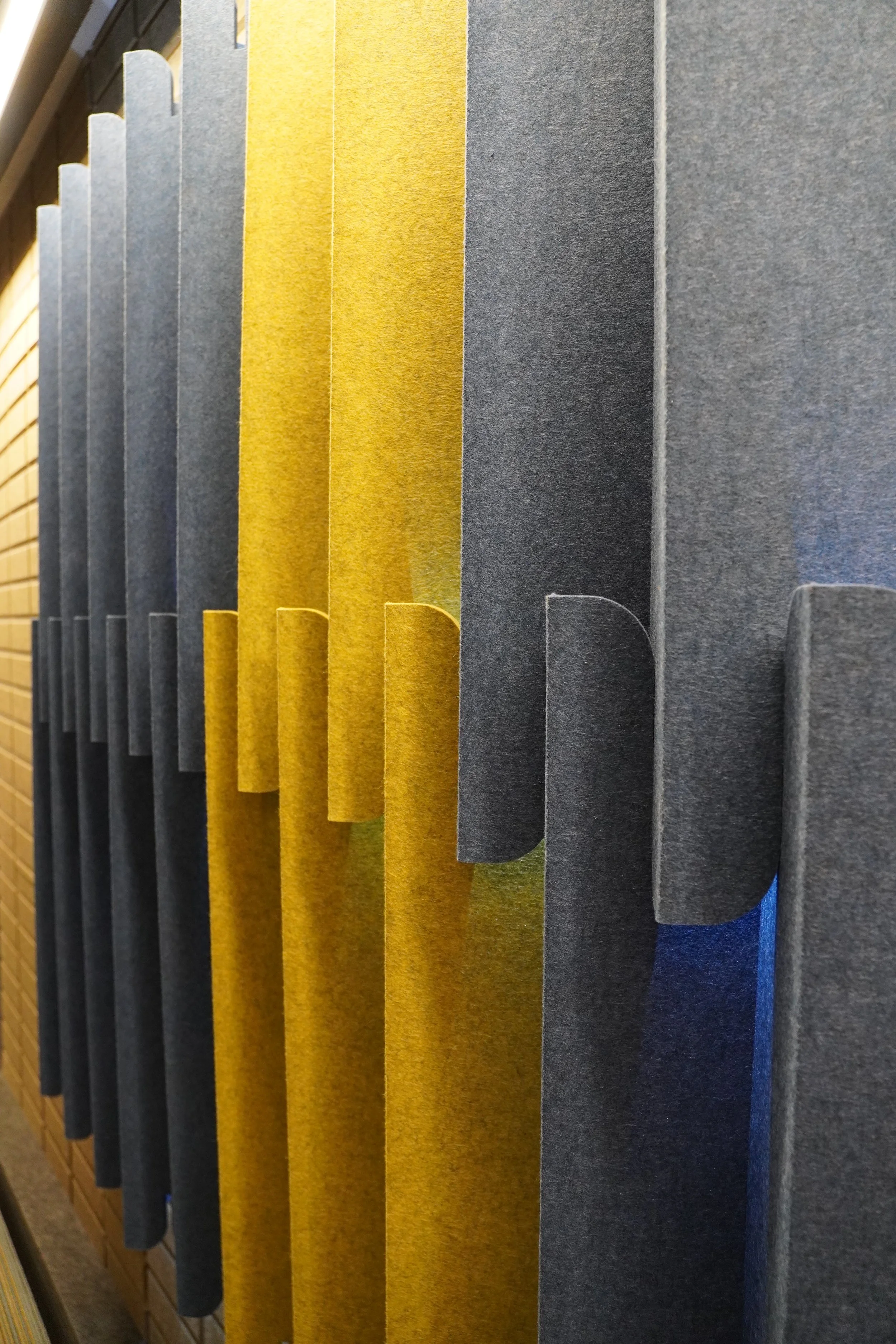 Close-up of colorful fabric or acoustic panels arranged vertically in navy, mustard yellow, gray, and brown colors.