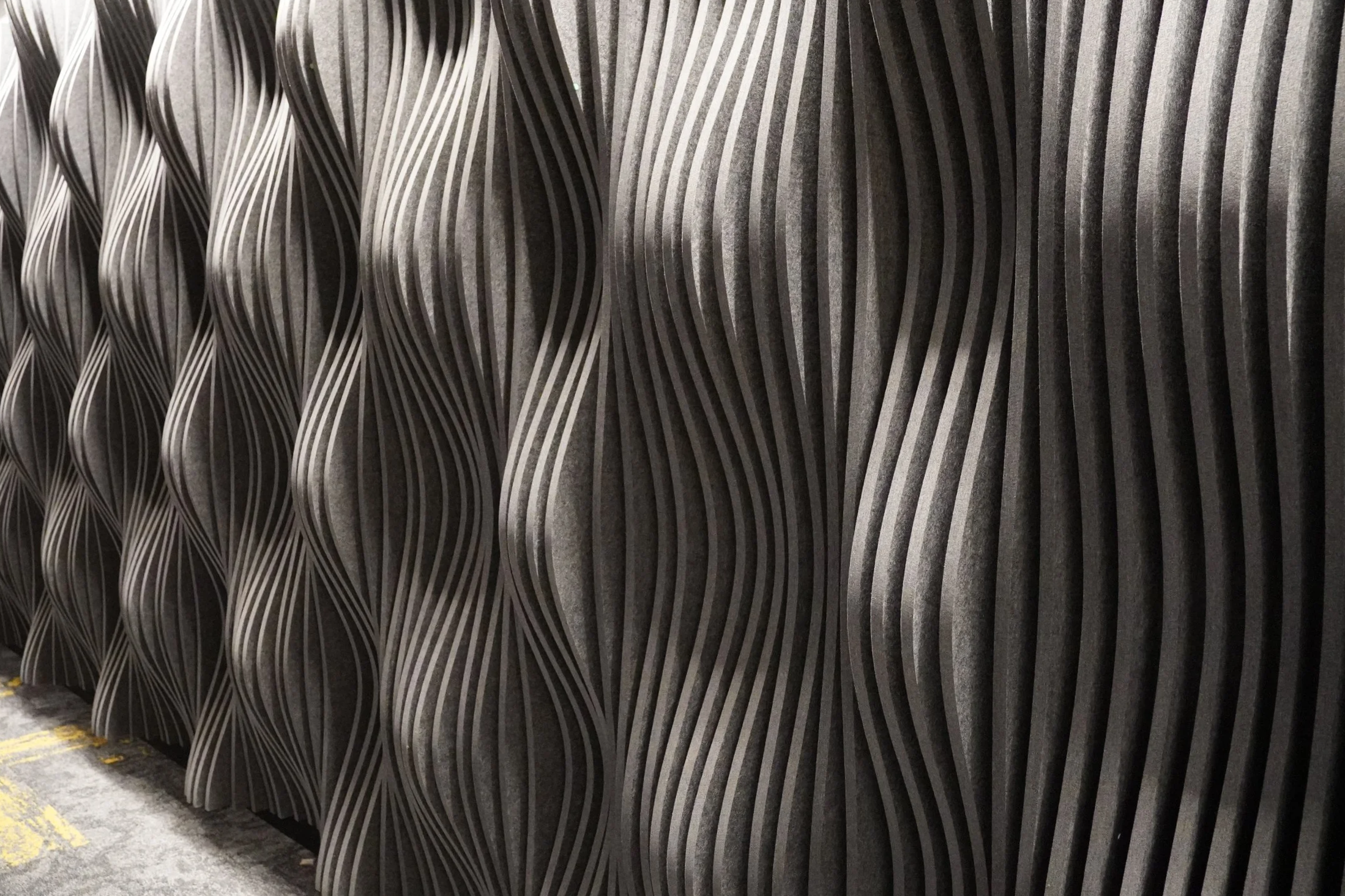 Abstract 3D wall sculpture made of black wavy vertical panels.