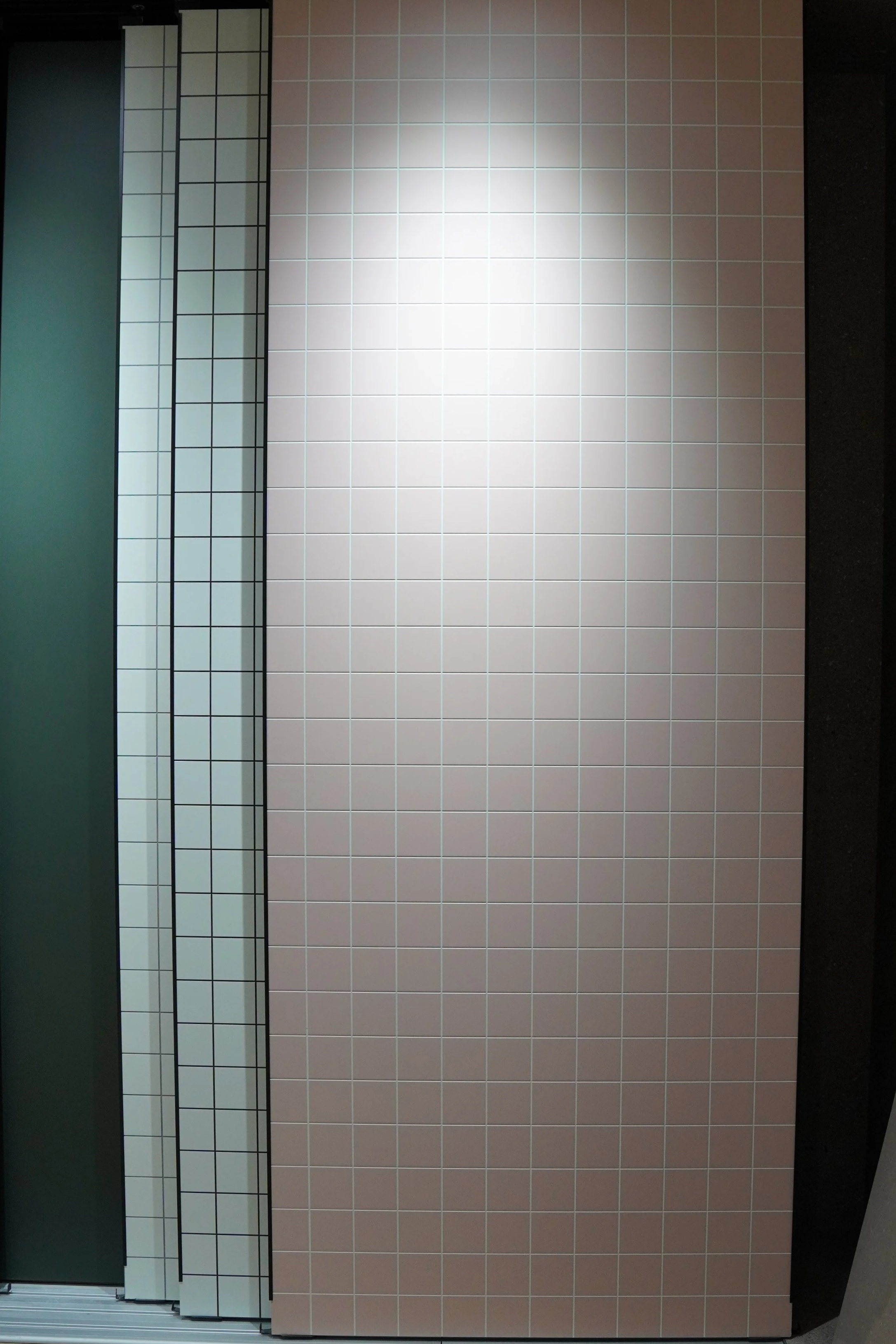 Display of different tiles, including small square white tiles with black grout lines, large beige tiles with light grout lines, and partial green tile section on the left.
