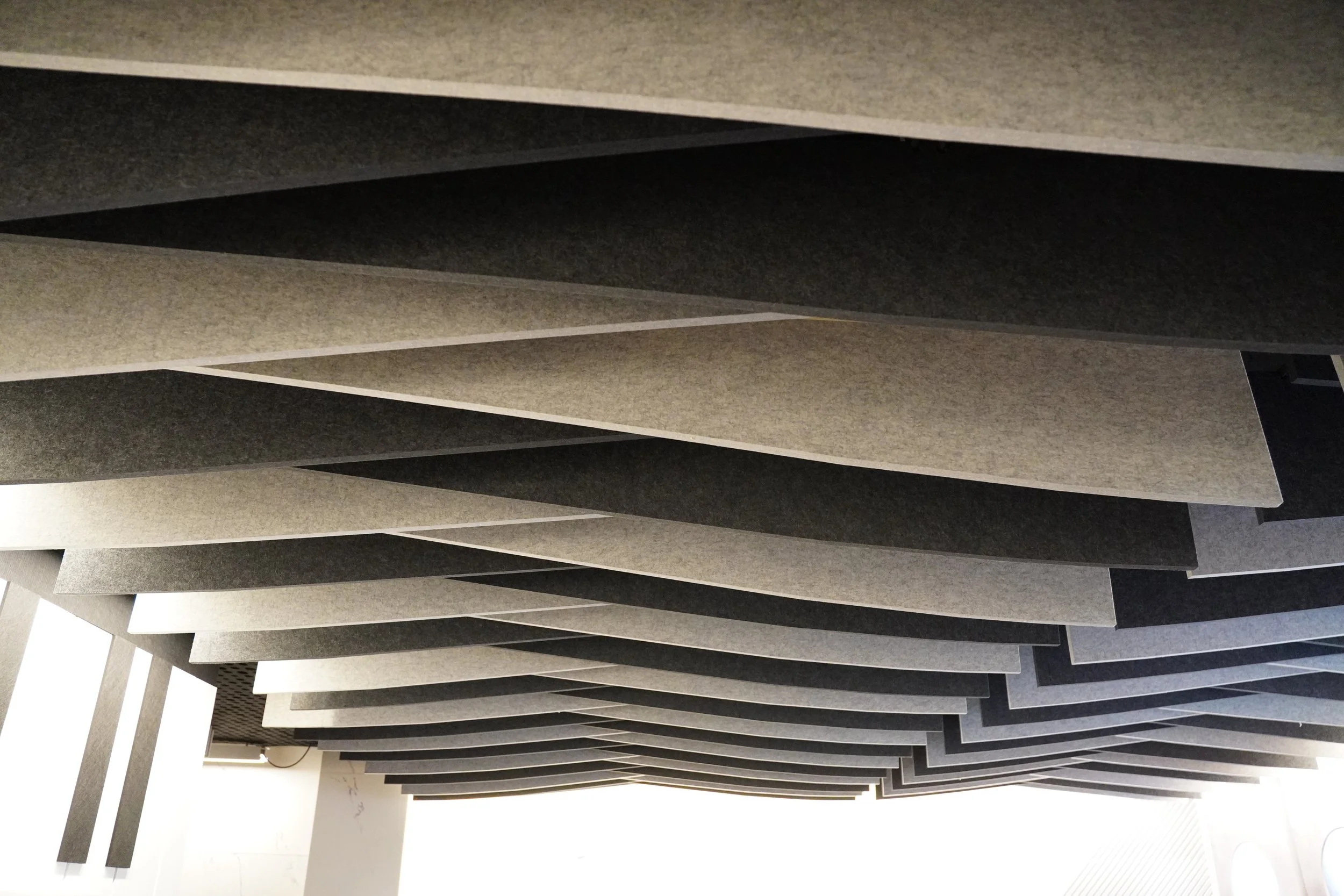 Ceiling with layered, staggered acoustic panels in shades of gray and black.