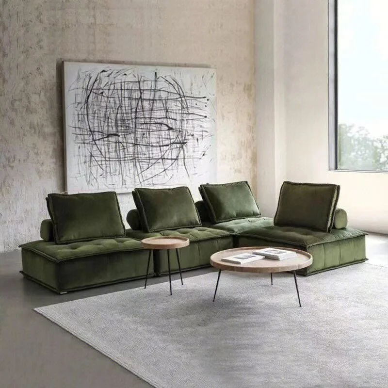 Modern living room with a green sectional sofa, a large abstract black and white painting, a window, and two small round coffee tables, one with magazines on it.