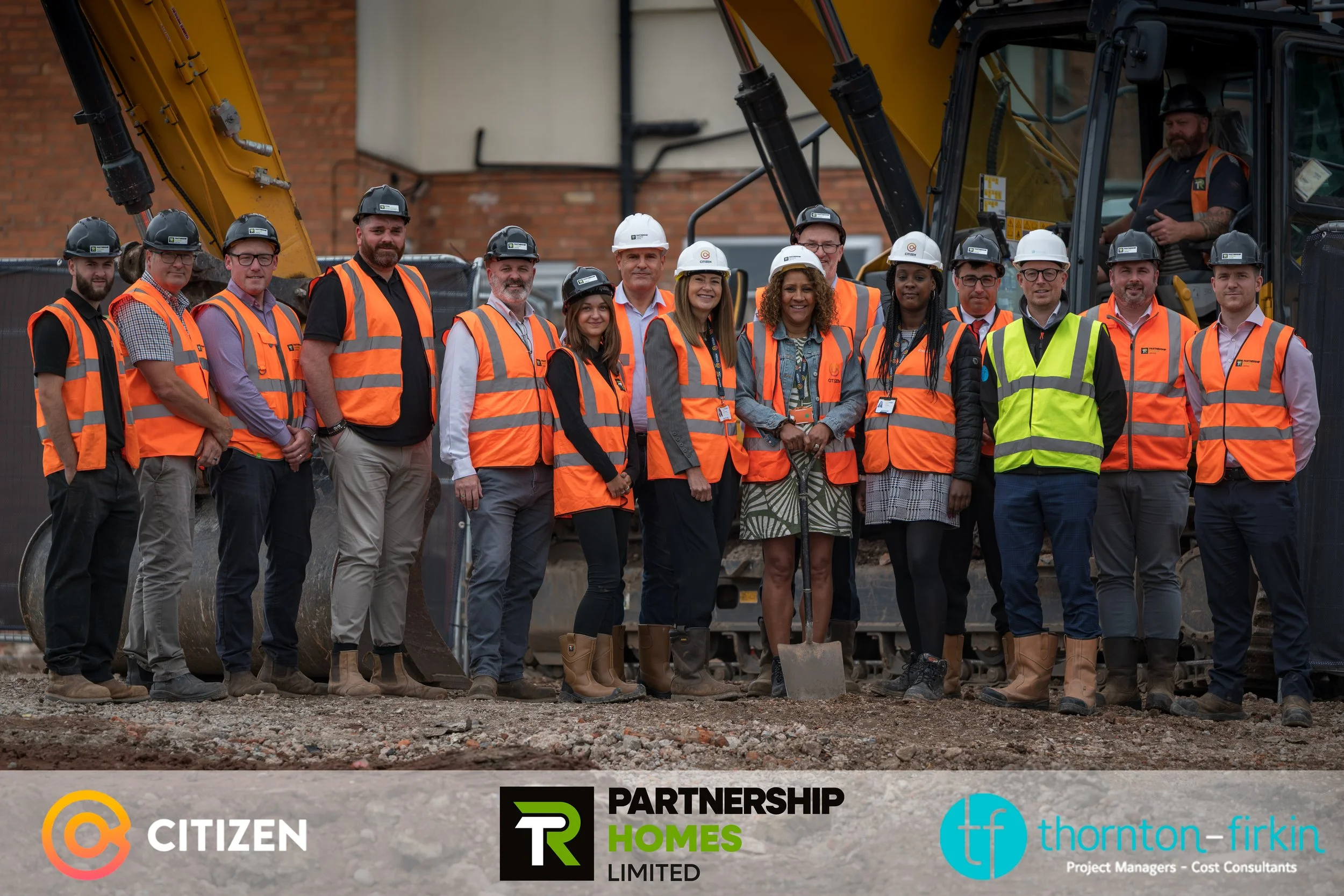 Group of construction workers and project managers in safety vests and helmets standing in front of construction equipment at a site.
