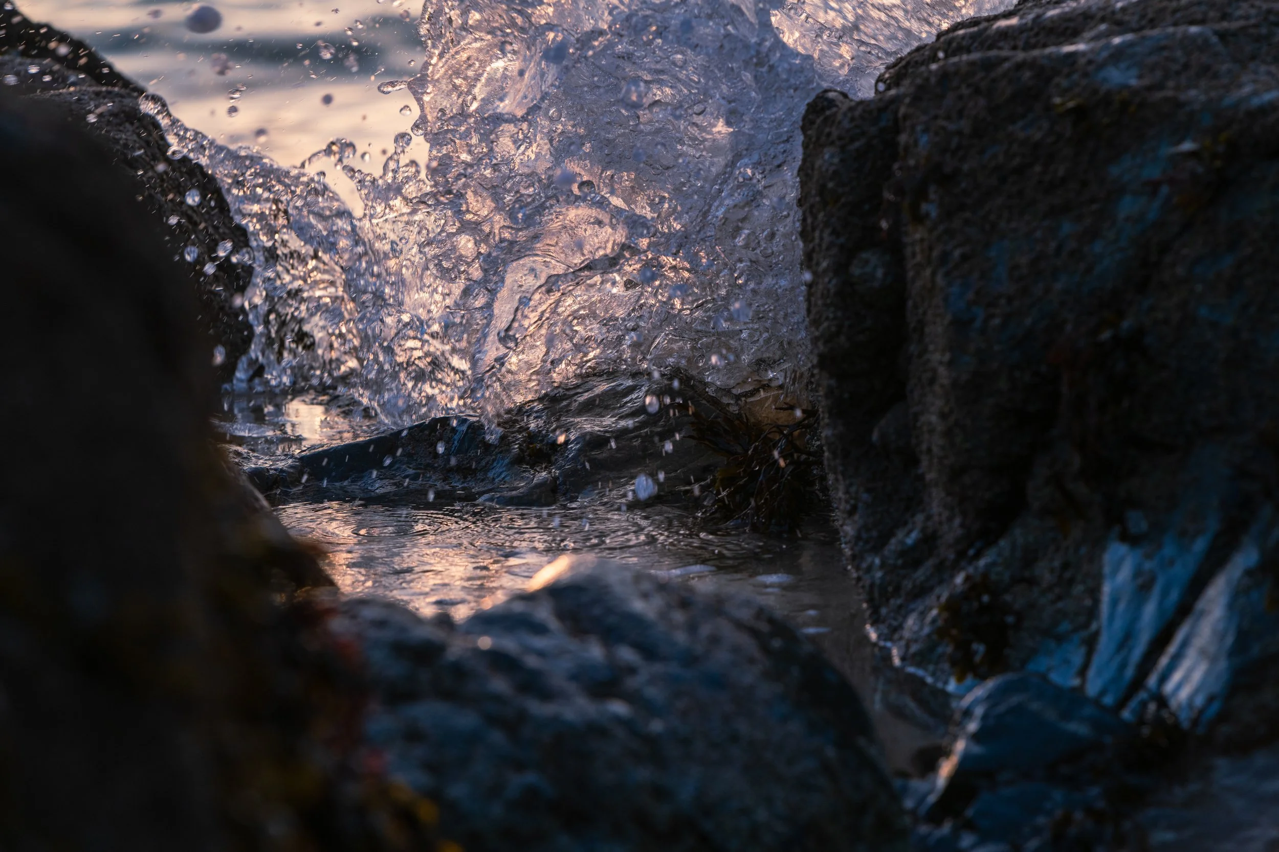 Close-up of water splashing among rocks at sunset.