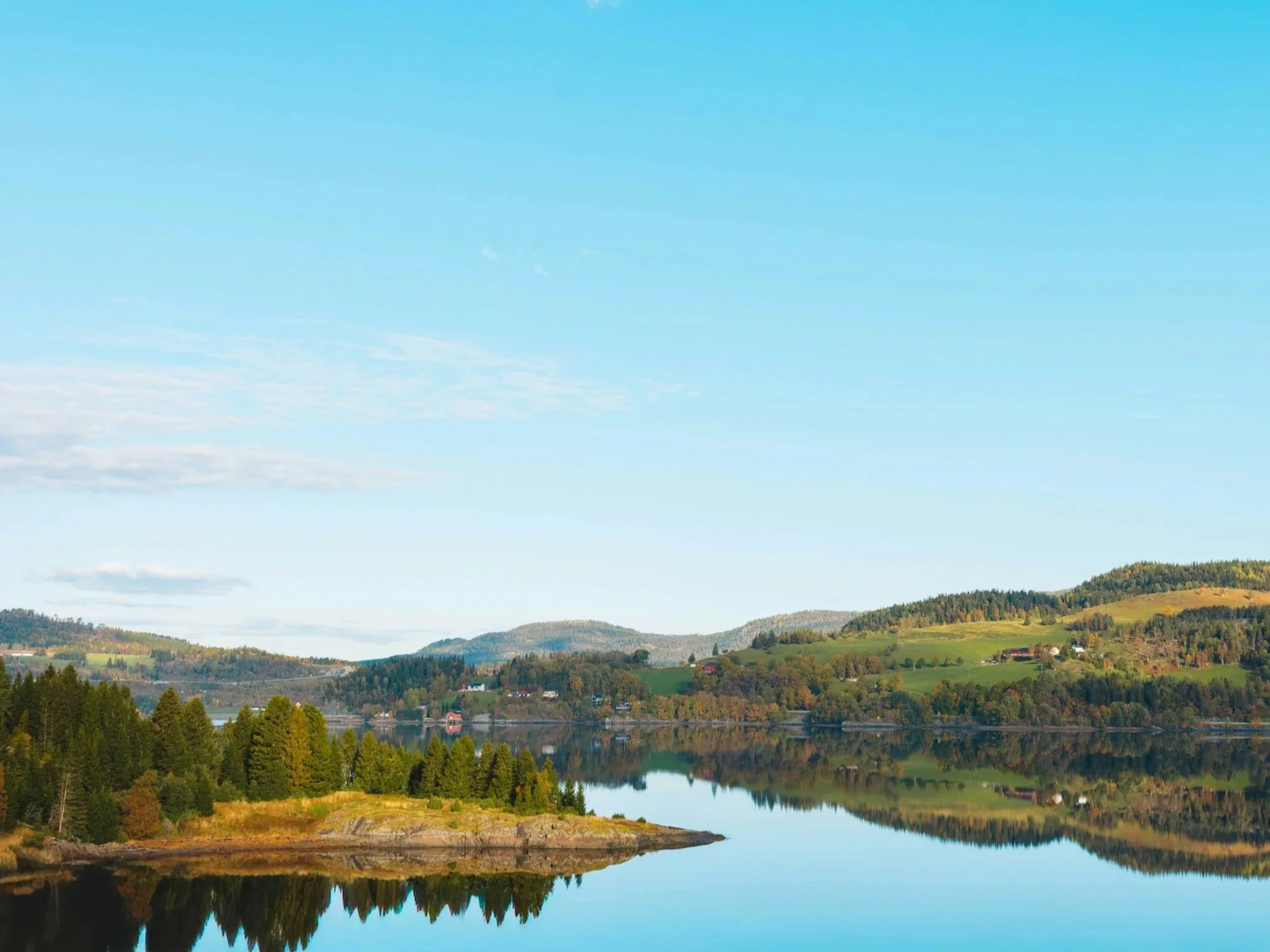 Calm lake surrounded by green hills and trees under a clear blue sky.