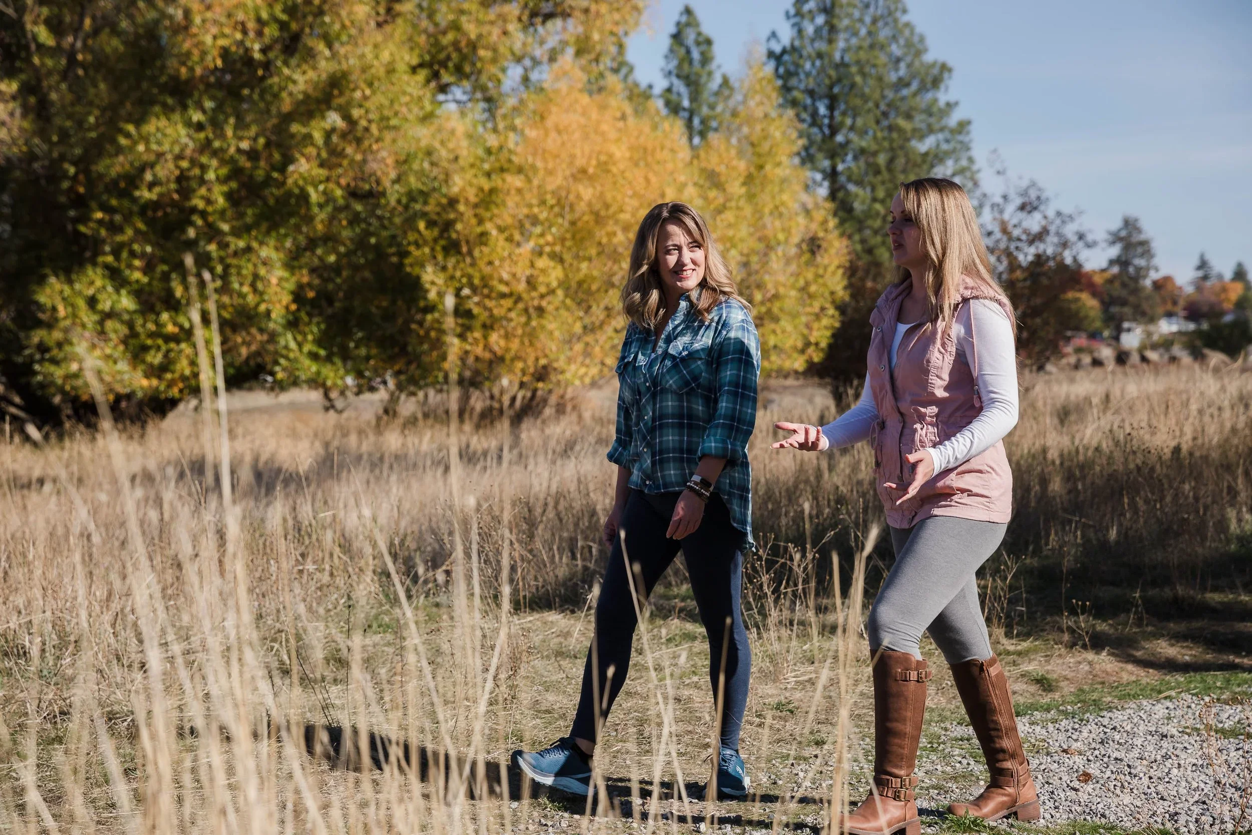 Two women walking and talking in a grassy field with trees showing autumn colors in the background.
