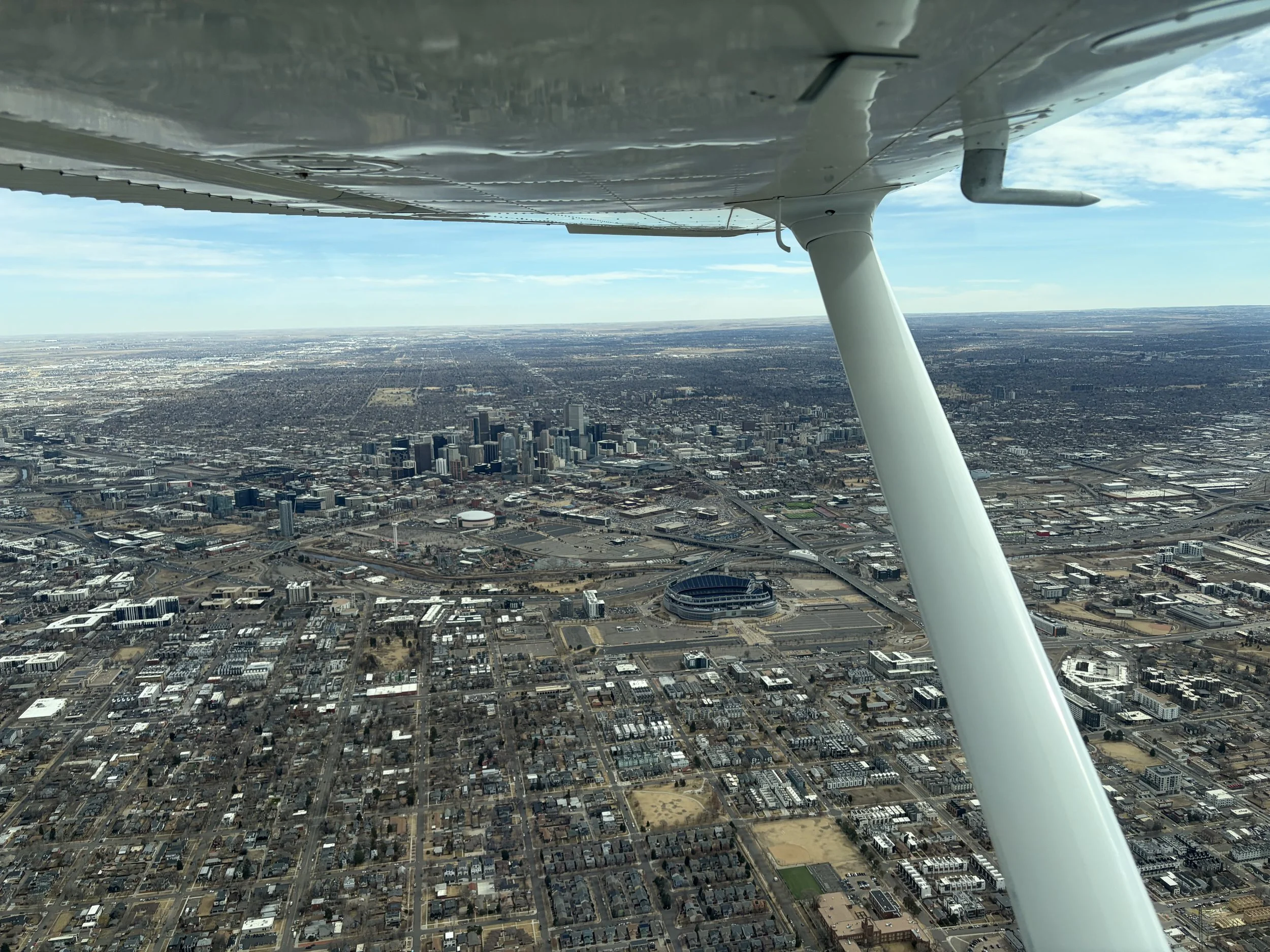 Aerial view from an airplane of a city with a stadium and tall buildings underneath.