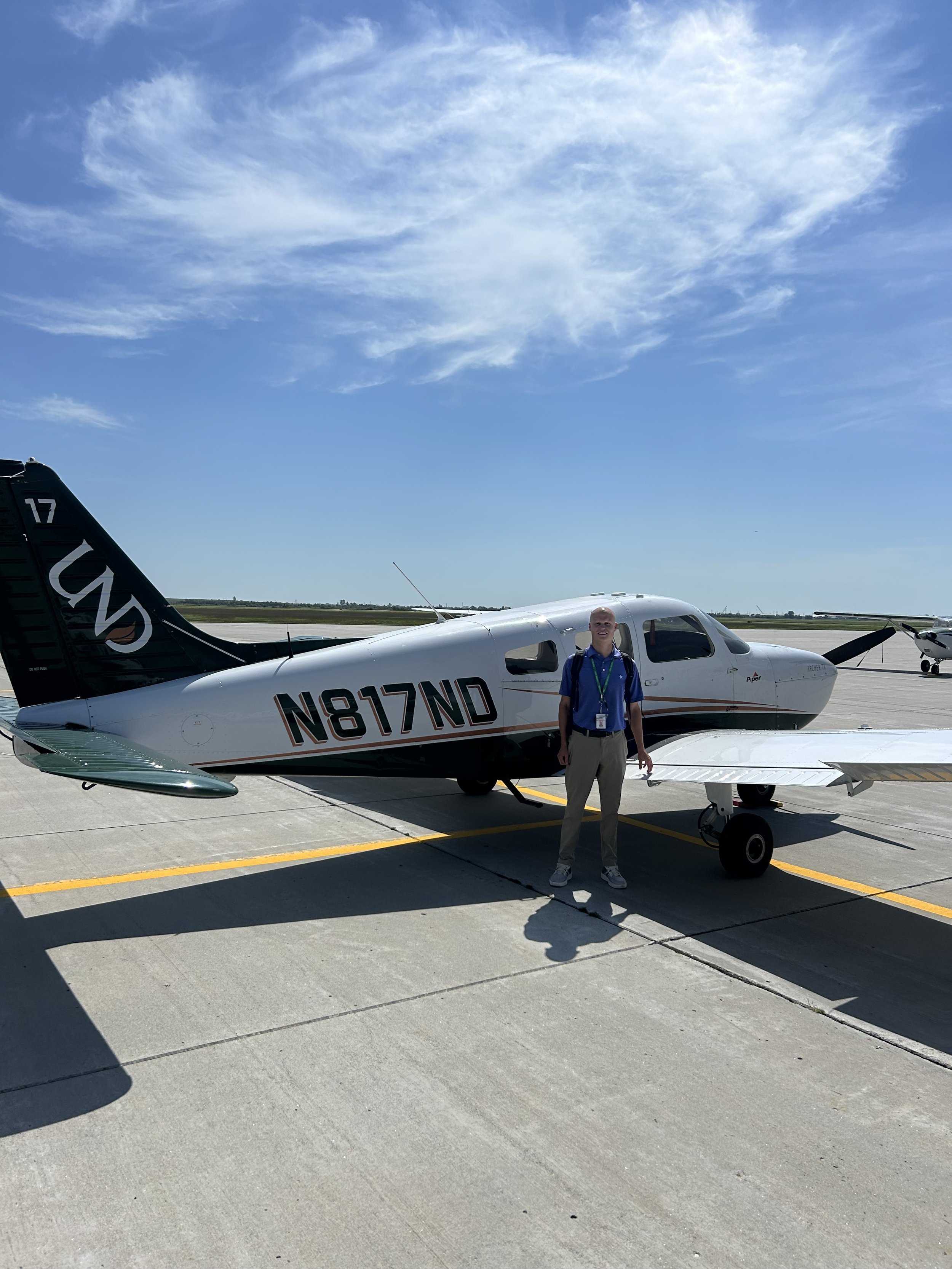 Person standing on airport tarmac next to small private airplane with tail number N817ND under a partly cloudy blue sky.