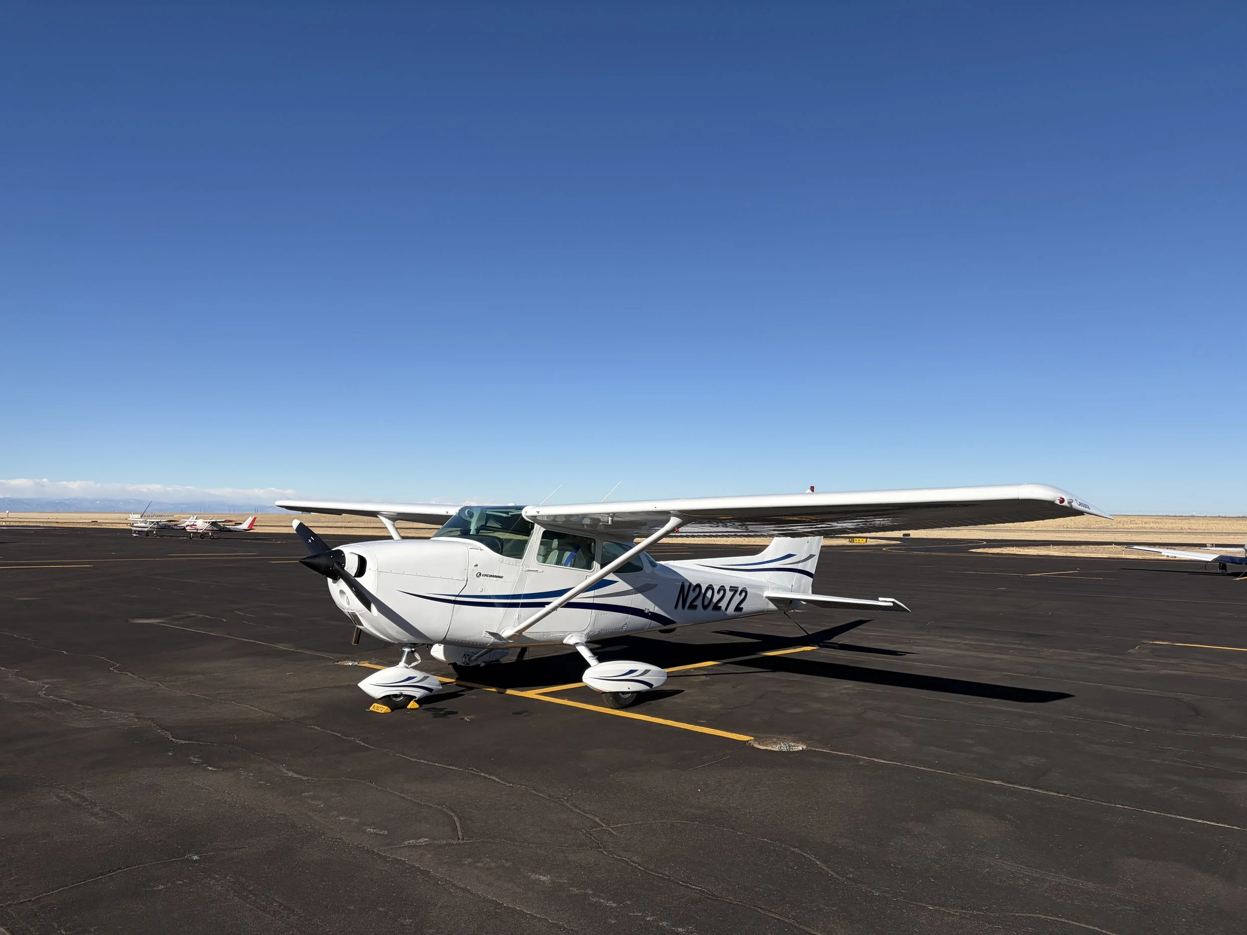 Small white airplane with blue stripes parked on an airport tarmac with a clear blue sky