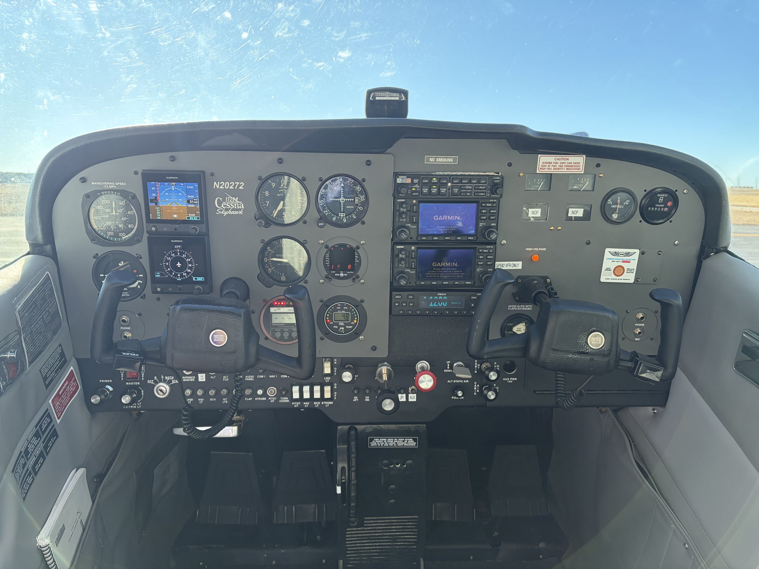 Interior cockpit of a small aircraft with various instruments, gauges, and screens, including GPS and communication devices.