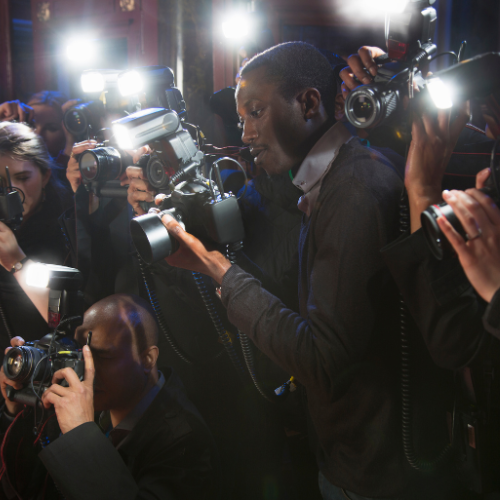 A man surrounded by photographers taking pictures in a crowded setting with bright flashes.