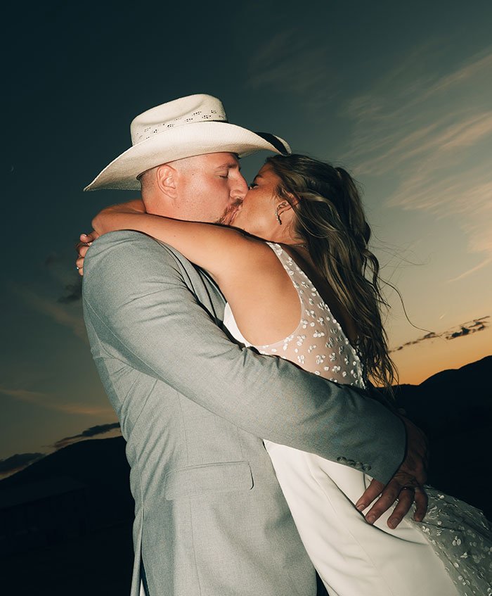 A groom kissing his bride during a Montana sunset wedding reception.