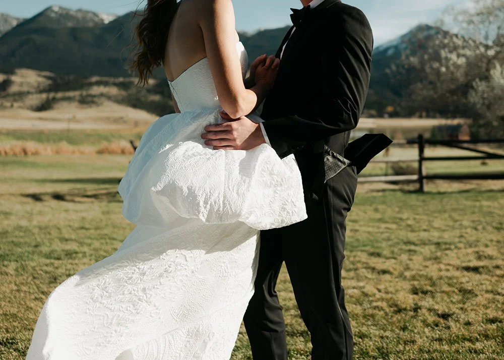 A bride and groom holding each other outdoors with a mountainous landscape in the background.