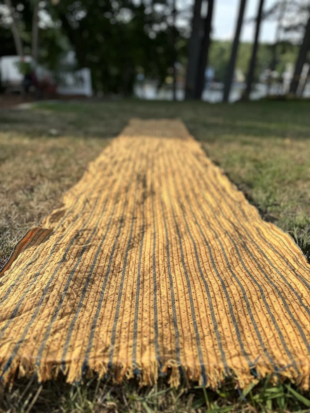 A yellow and black striped fabric mat laid on grass outdoors, with a blurred background of trees and a fence.