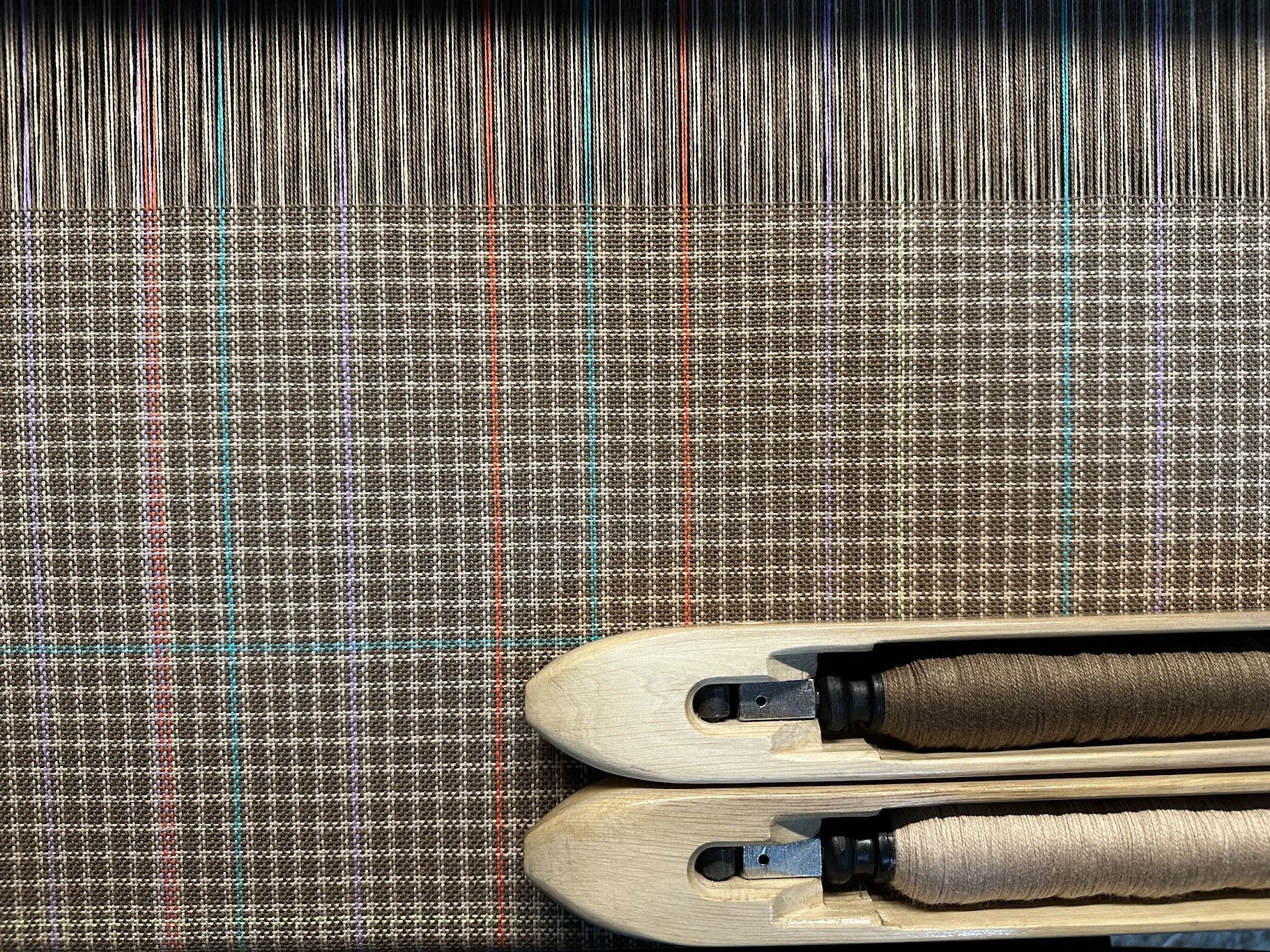 Close-up of two antique wooden weaving shuttles with woven fabric in the background.