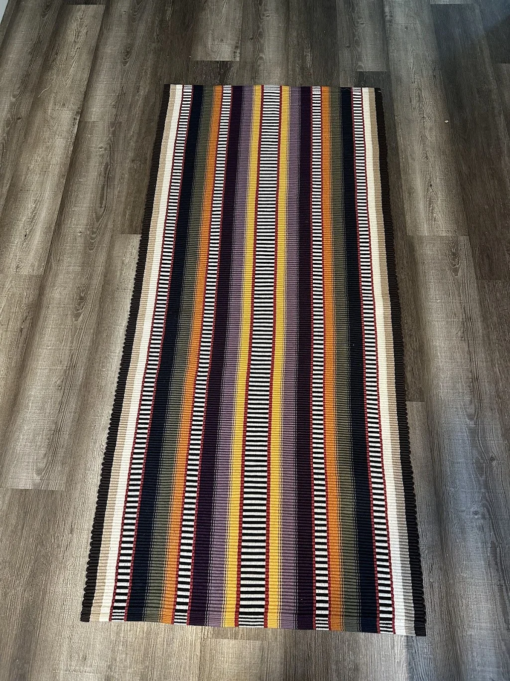 Colorful striped rug on a gray wood floor.