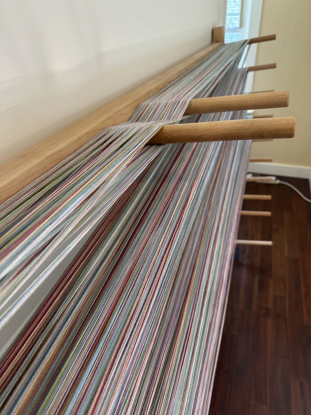Close-up of a wooden loom with colorful striped fabric woven on it, placed along the wall in a room.