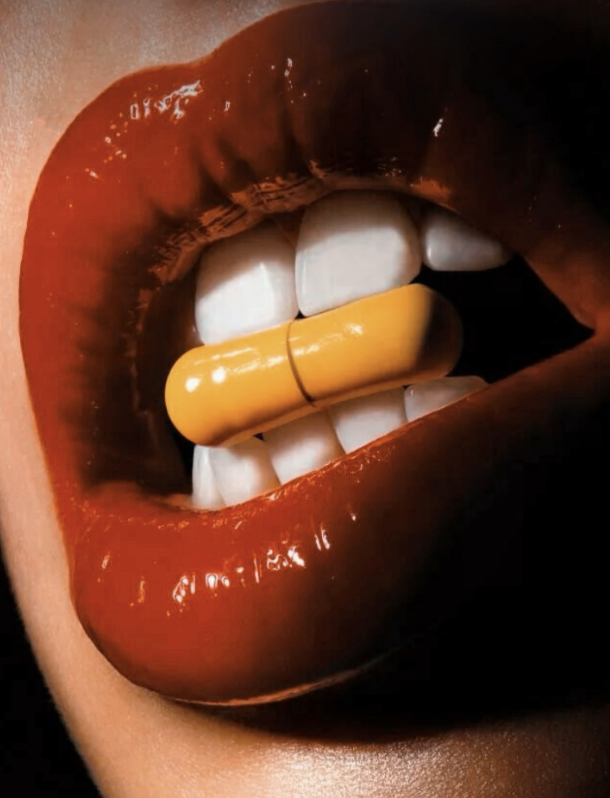 Close-up of lips with dark lipstick, teeth biting a yellow capsule pill.