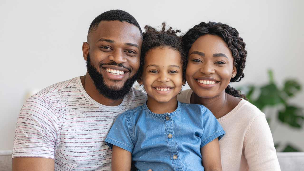 Une famille de trois personnes souriantes, un père, une mère et une fille, posant ensemble à l'intérieur.