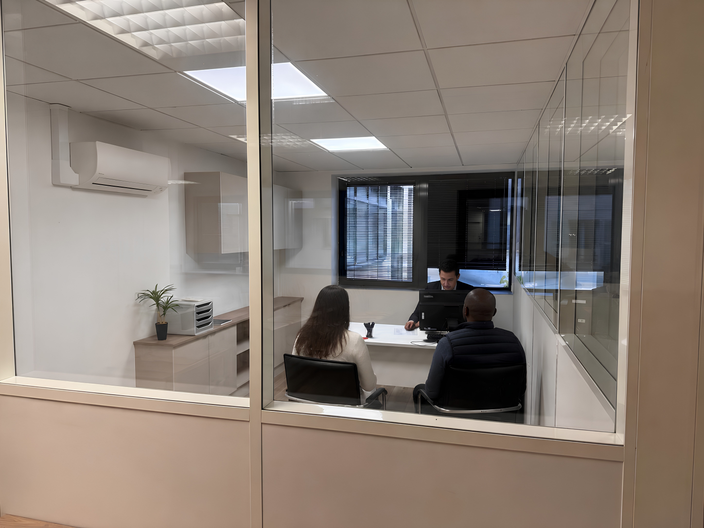 Une salle de réunion avec trois personnes en pleine discussion, vue à travers une vitre.
