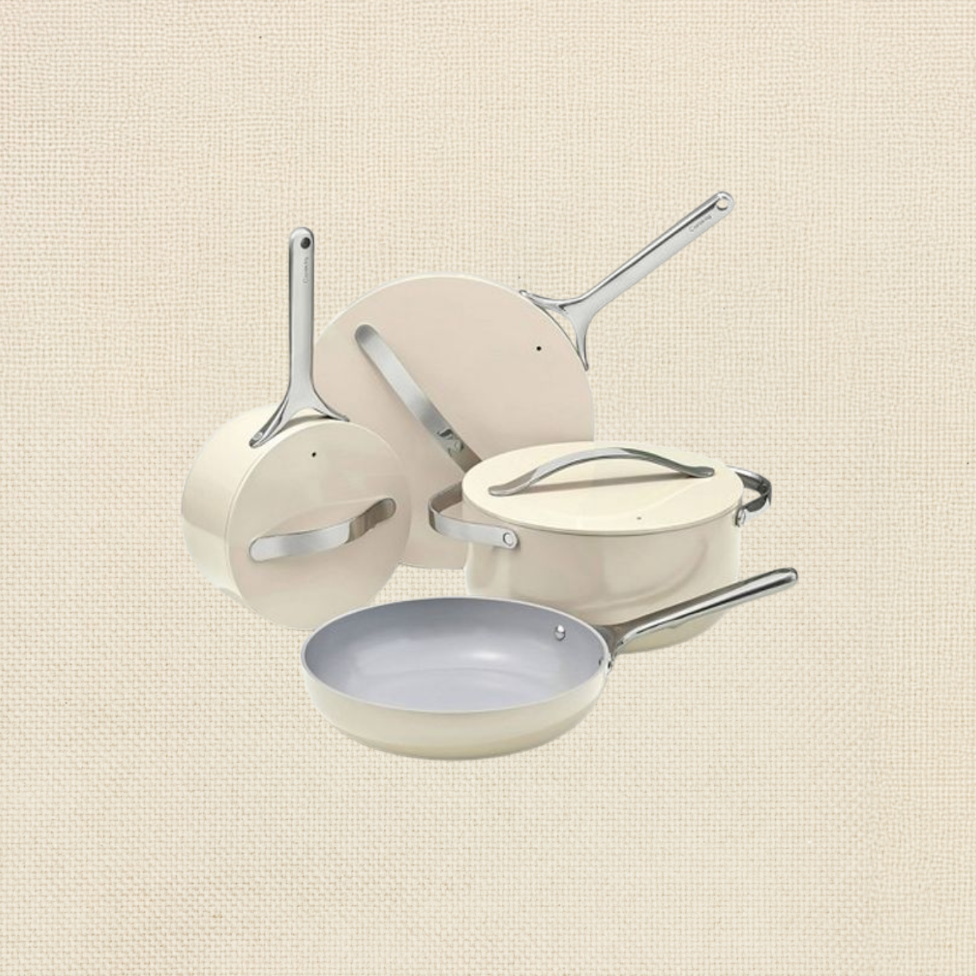 Set of cream-colored kitchen cookware including frying pans, saucepans, and a pot with lids, arranged together against a textured beige background.