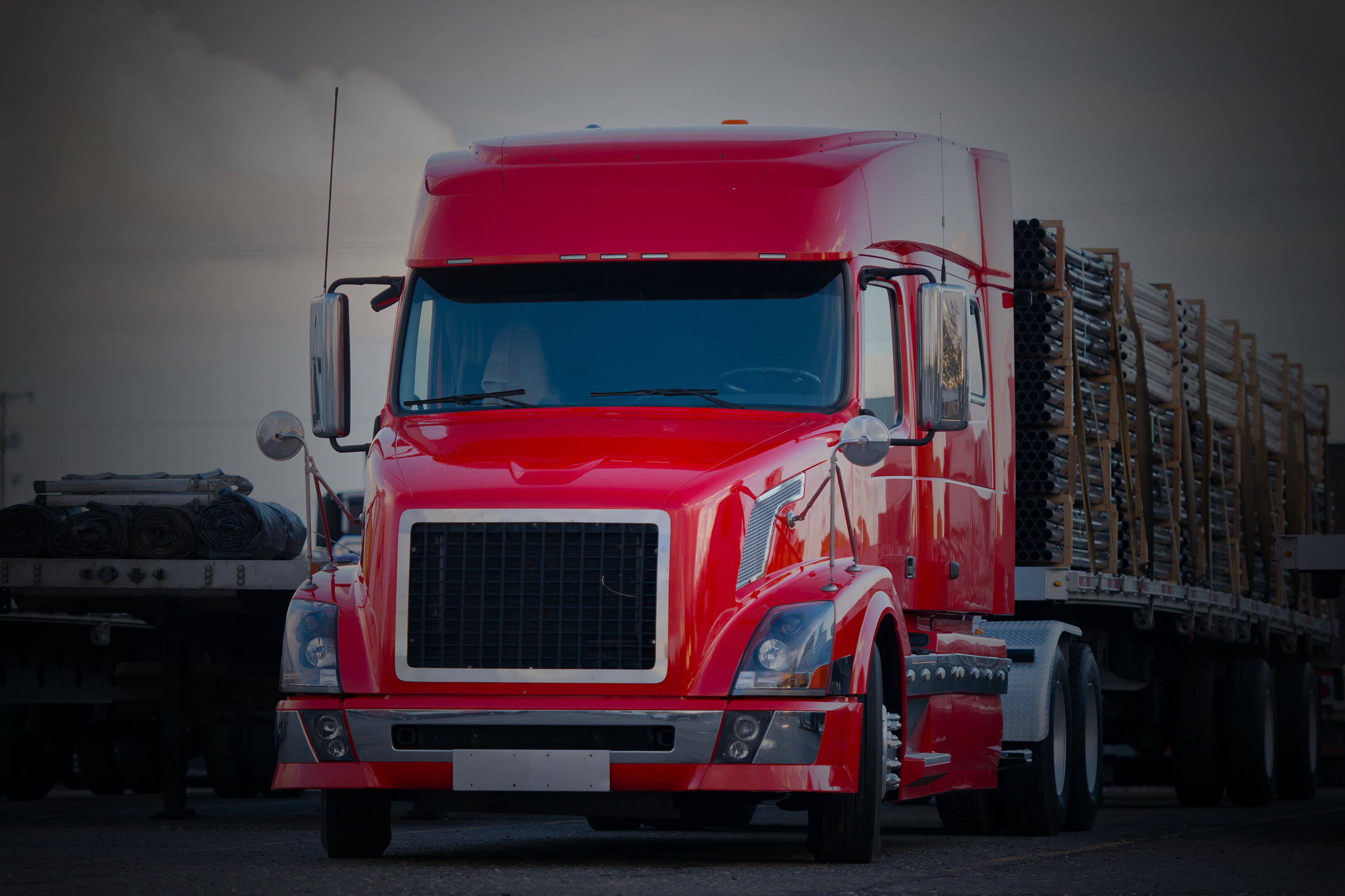 A red semi-truck hauling pipes on a trailer.