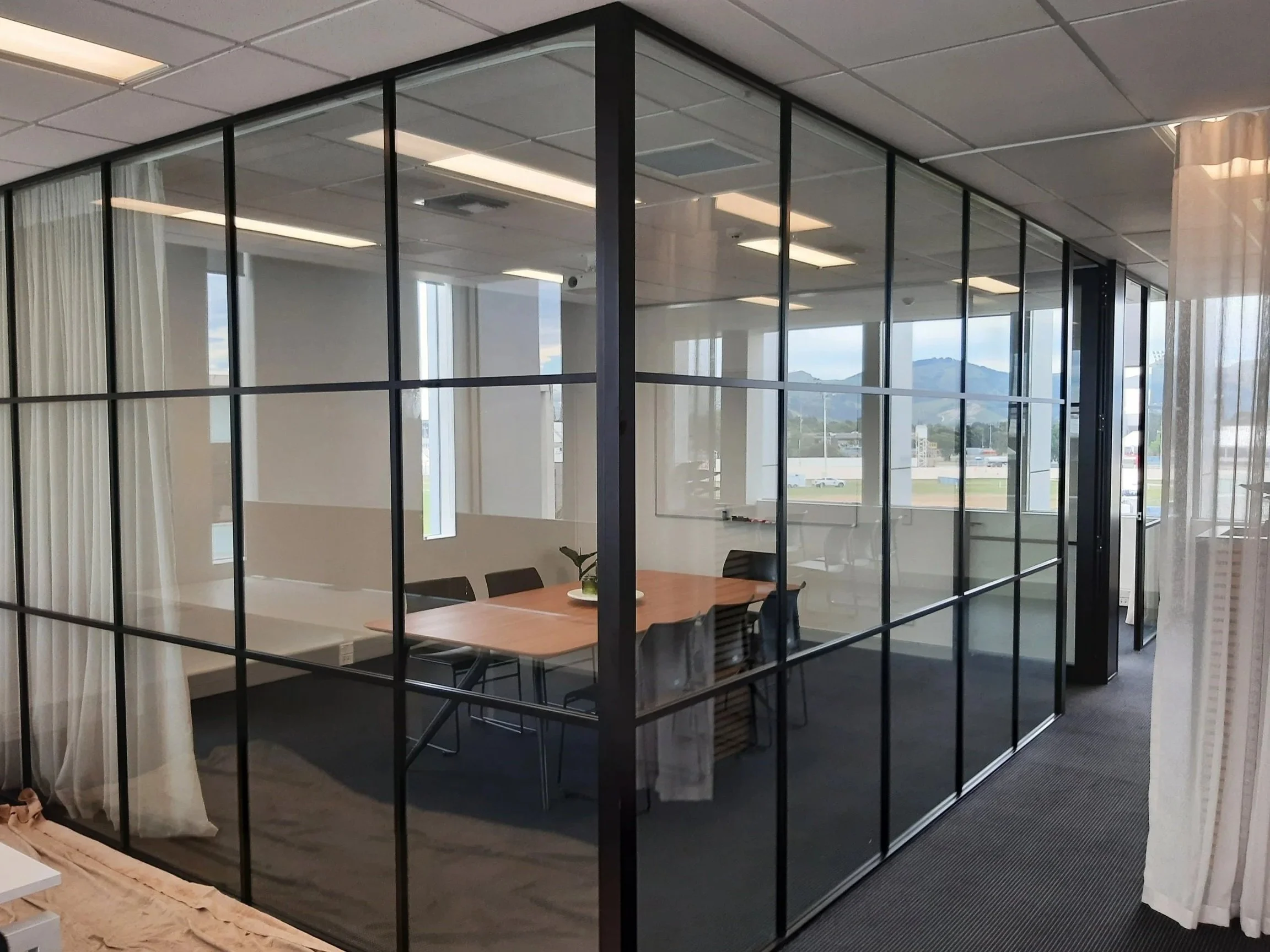 Modern glass-enclosed conference room with a wooden table, black chairs, and view of mountains through large windows