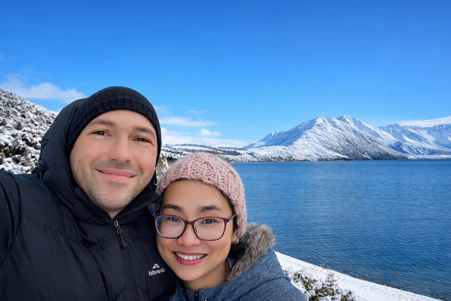 The founders of glacierlite joinery & glazing ltd in a selfie in winter near a snow-covered landscape with mountains and a lake in the background.