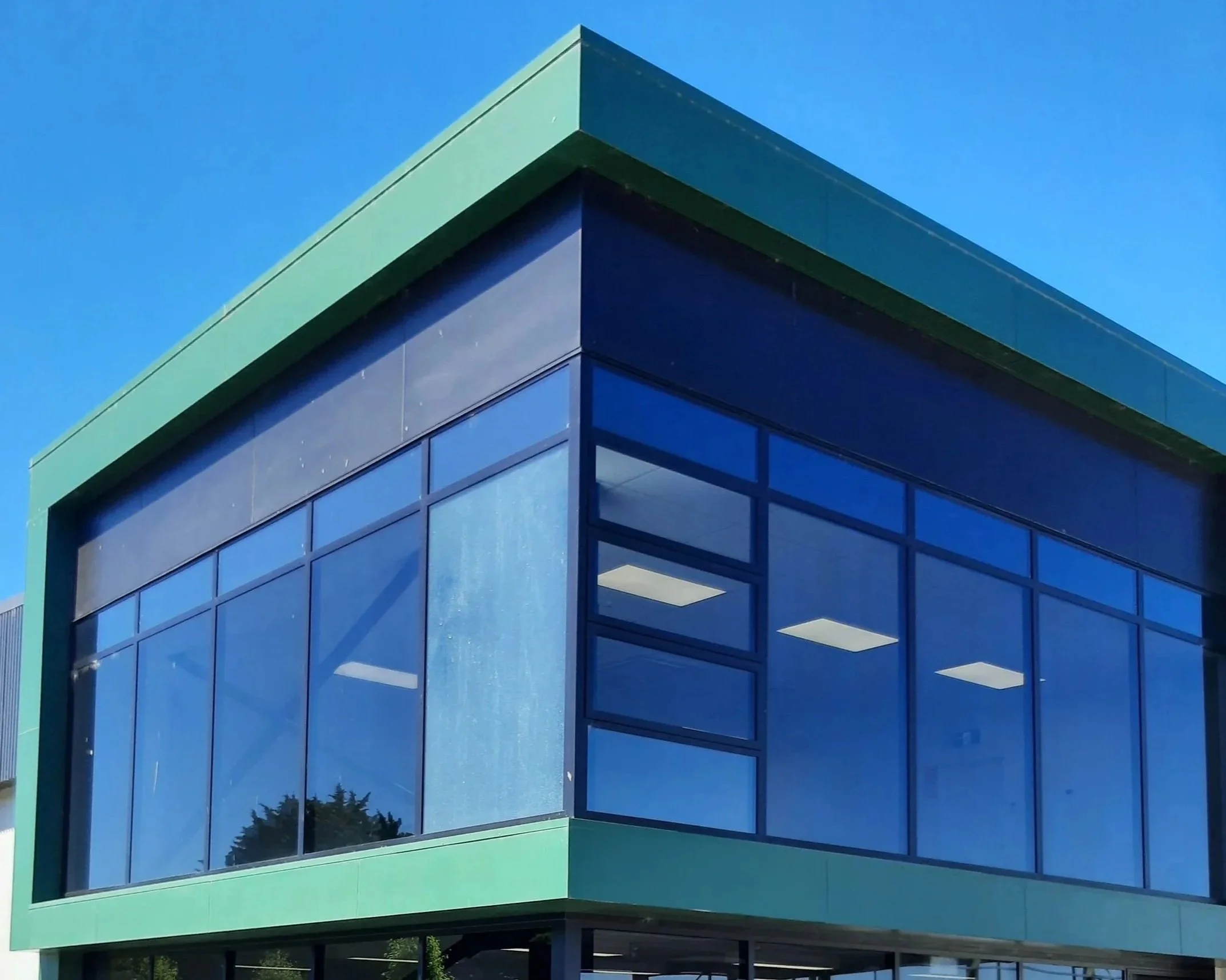 Modern building with large glass windows and green framing, under a clear blue sky.