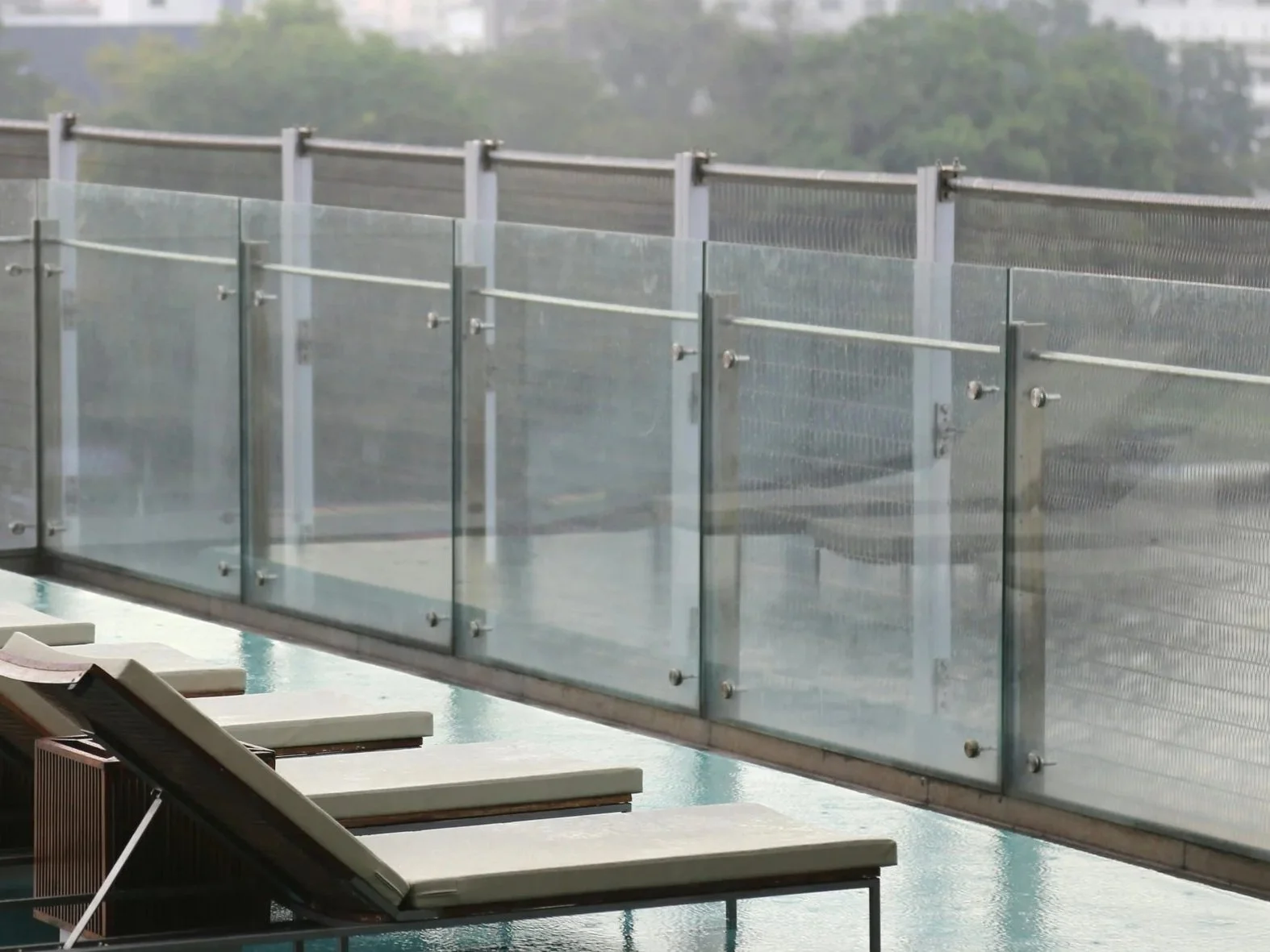 Empty lounge chairs beside a swimming pool, with a glass and metal railing in the background.
