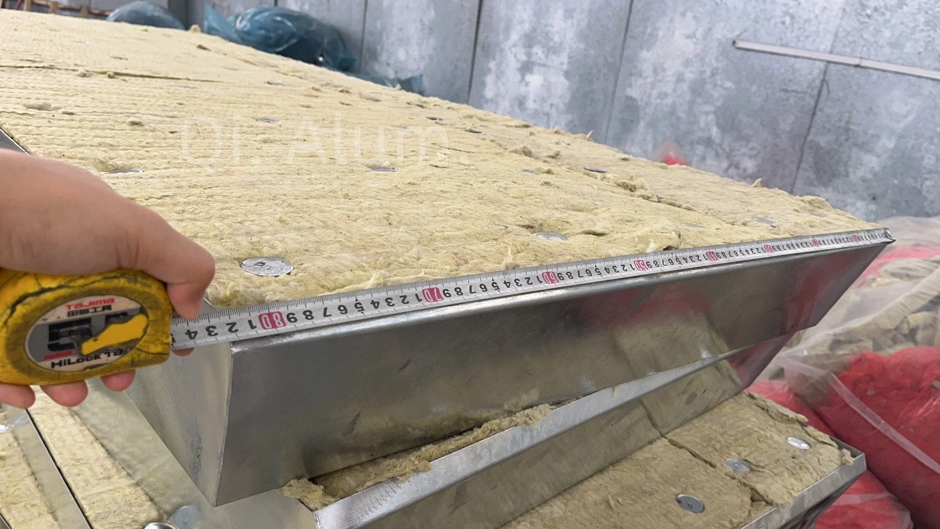 Person measuring insulation material with a measuring tape, on a metal surface, in a construction or renovation setting.