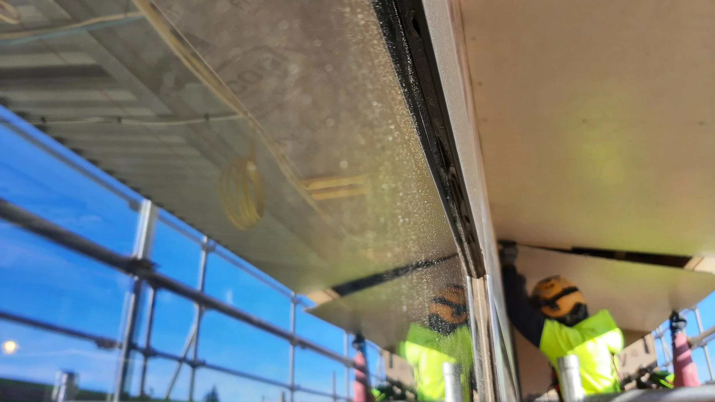Worker in a high-visibility yellow vest and helmet installing or repairing a large retrofit double glazing external window