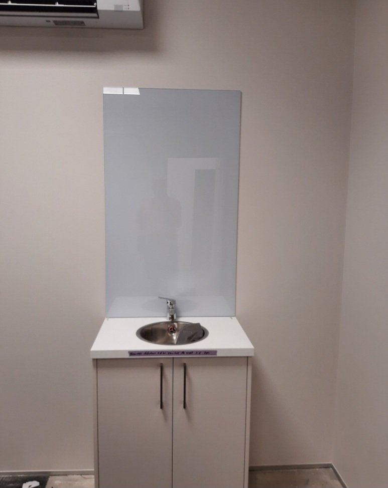 Small white sink cabinet with a stainless steel basin and a faucet, located against a light-colored wall, with a mirror or panel behind it.