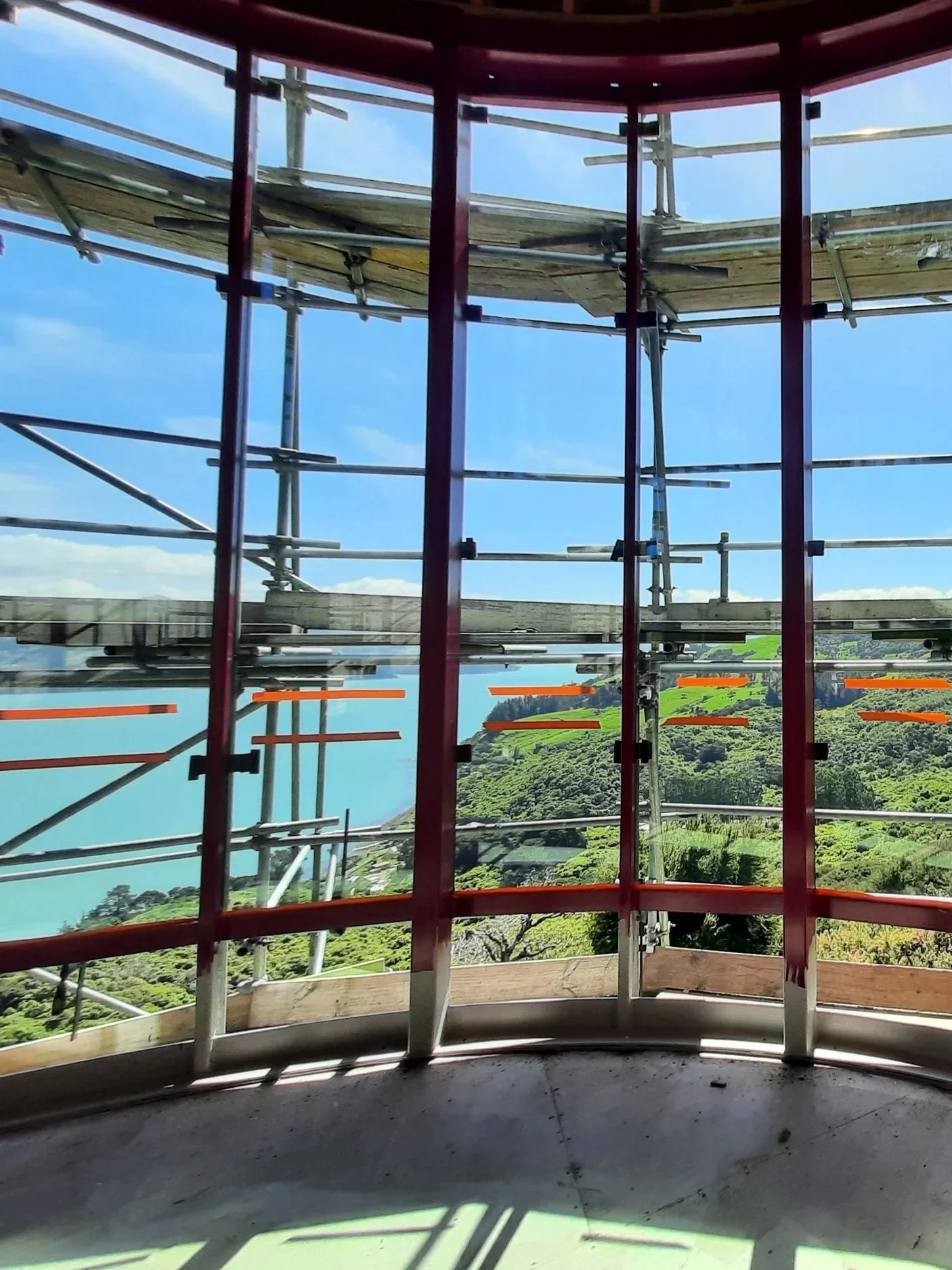 View through window frames and joinery, overlooking a lake surrounded by green hills and trees under a partly cloudy sky.