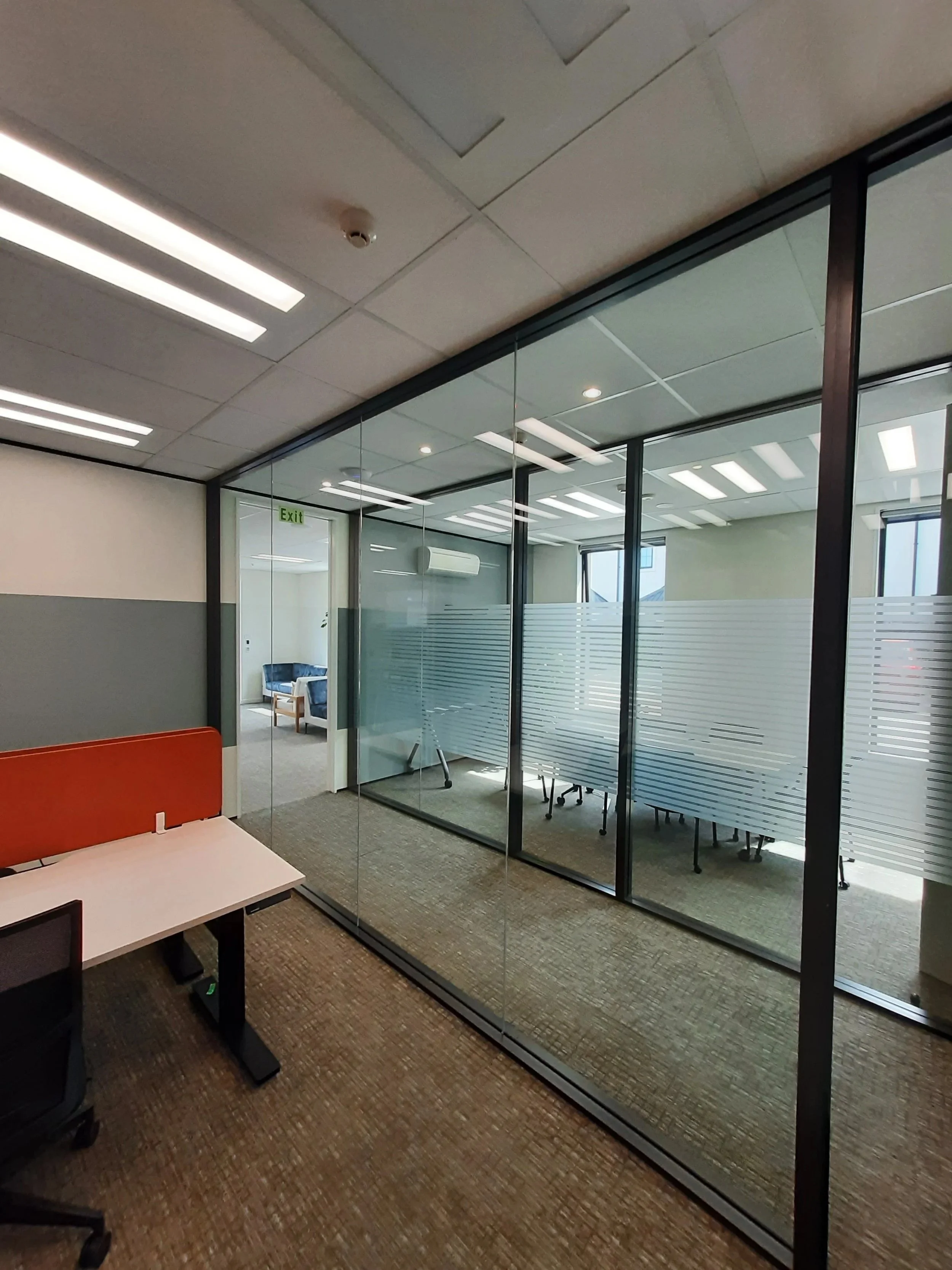 Office with glass-walled conference room and a desk with a red divider in the foreground.