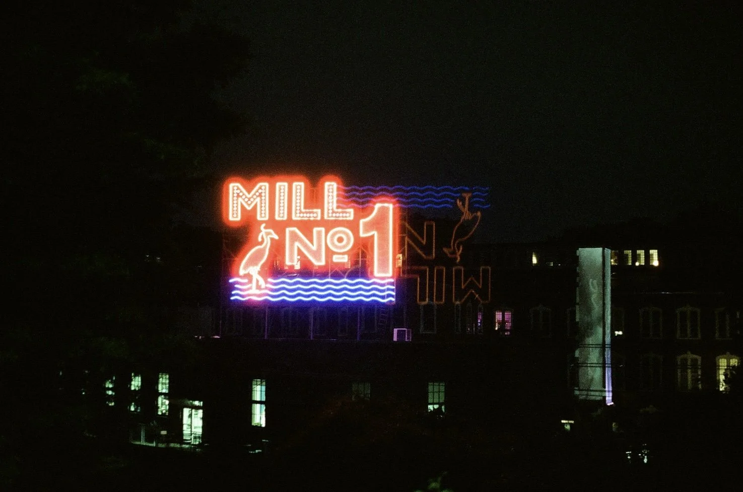 Neon sign reading 'MILL NO 1' with a pelican and a whale, set against a dark night sky.