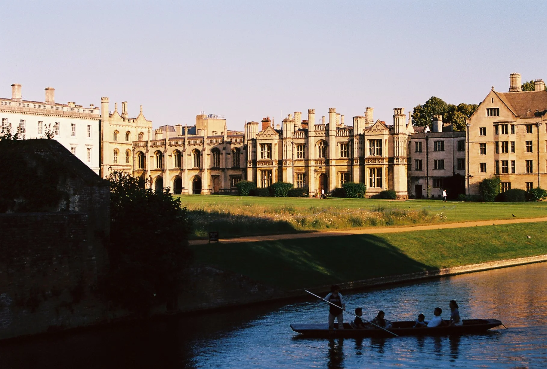 A group of five people in a boat on a river with a historic castle and green lawns in the background, during sunset.