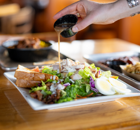 Salad topped with chicken and dressing being poured on top.