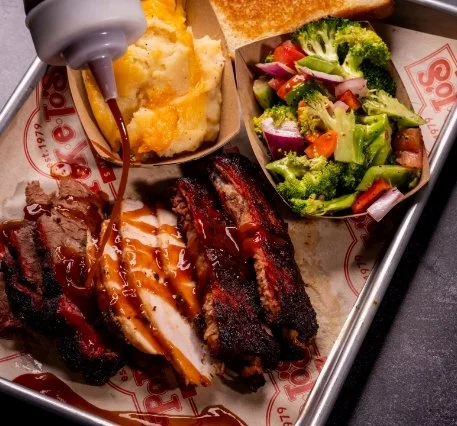 Three meat BBQ plate with assorted smoked meats and sides.