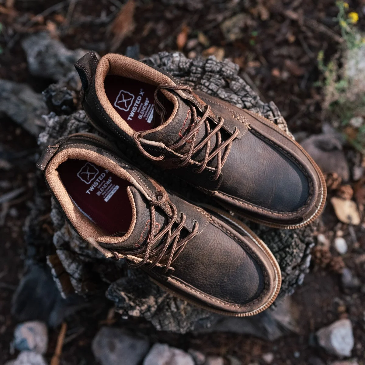 Pair of brown and black work boots resting on a piece of chopped wood outdoors.