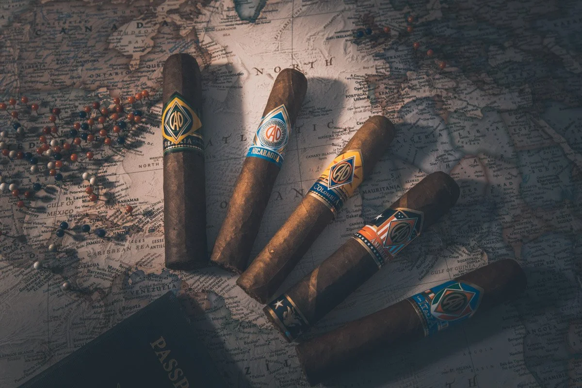 Five cigars with colorful bands laid on a world map, with scattered beads and a passport nearby.