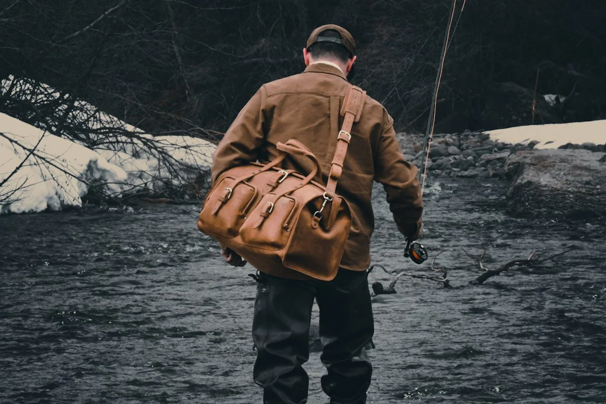 Man fly fishing in a river with snowy banks and leafless trees in the background.
