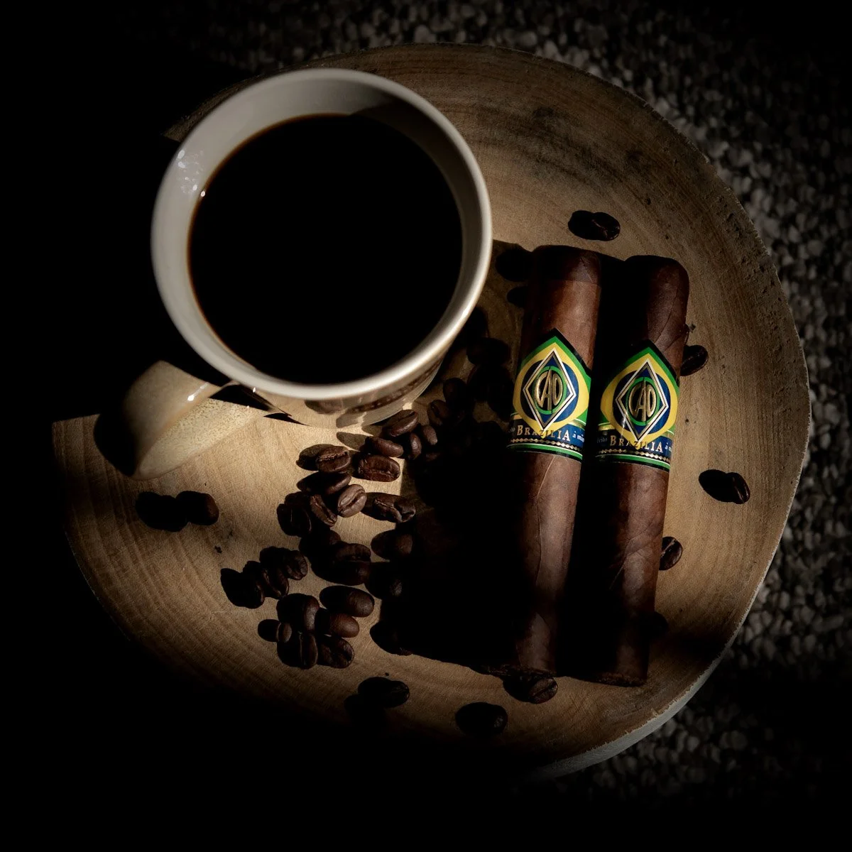A white mug filled with black coffee, two cigars with Brazilian labels, and scattered coffee beans on a round wooden tray.