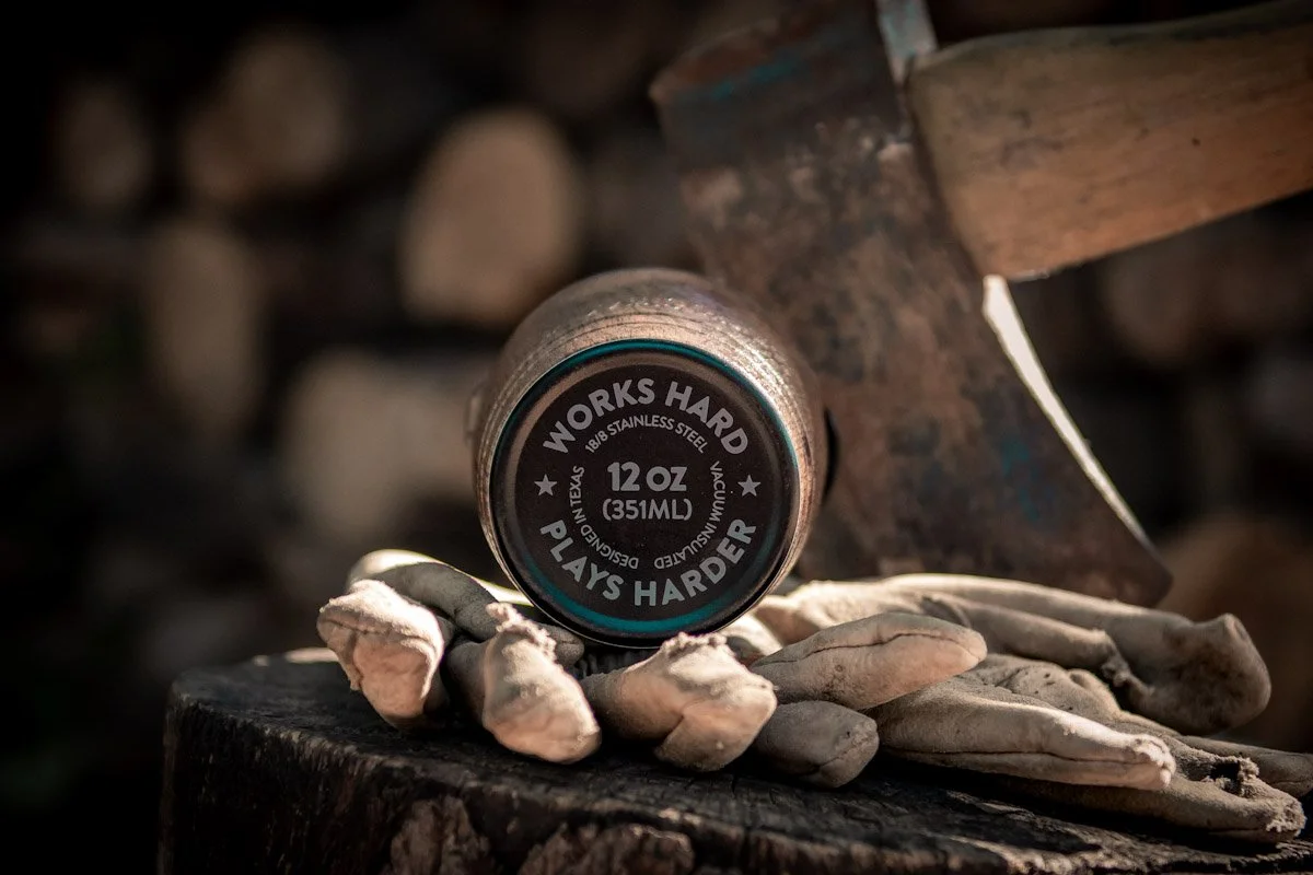 A can of wood stain on a tree stump with gloves nearby and chopped wood in the background.