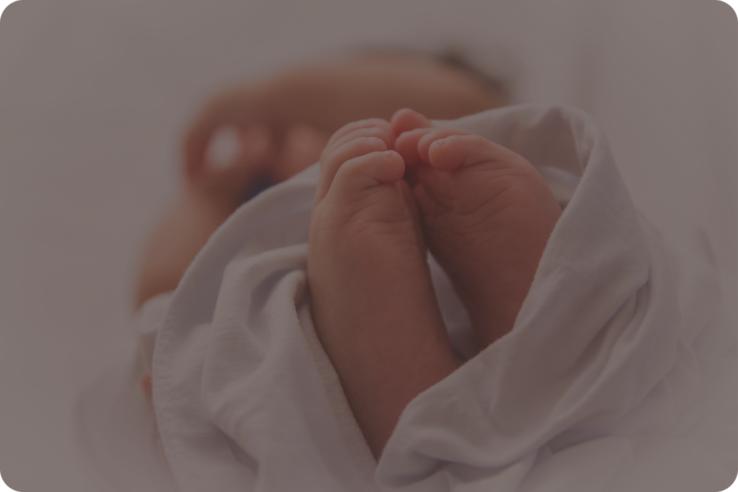 Close-up of a newborn baby's tiny feet touching, with the baby's face slightly out of focus in the background.