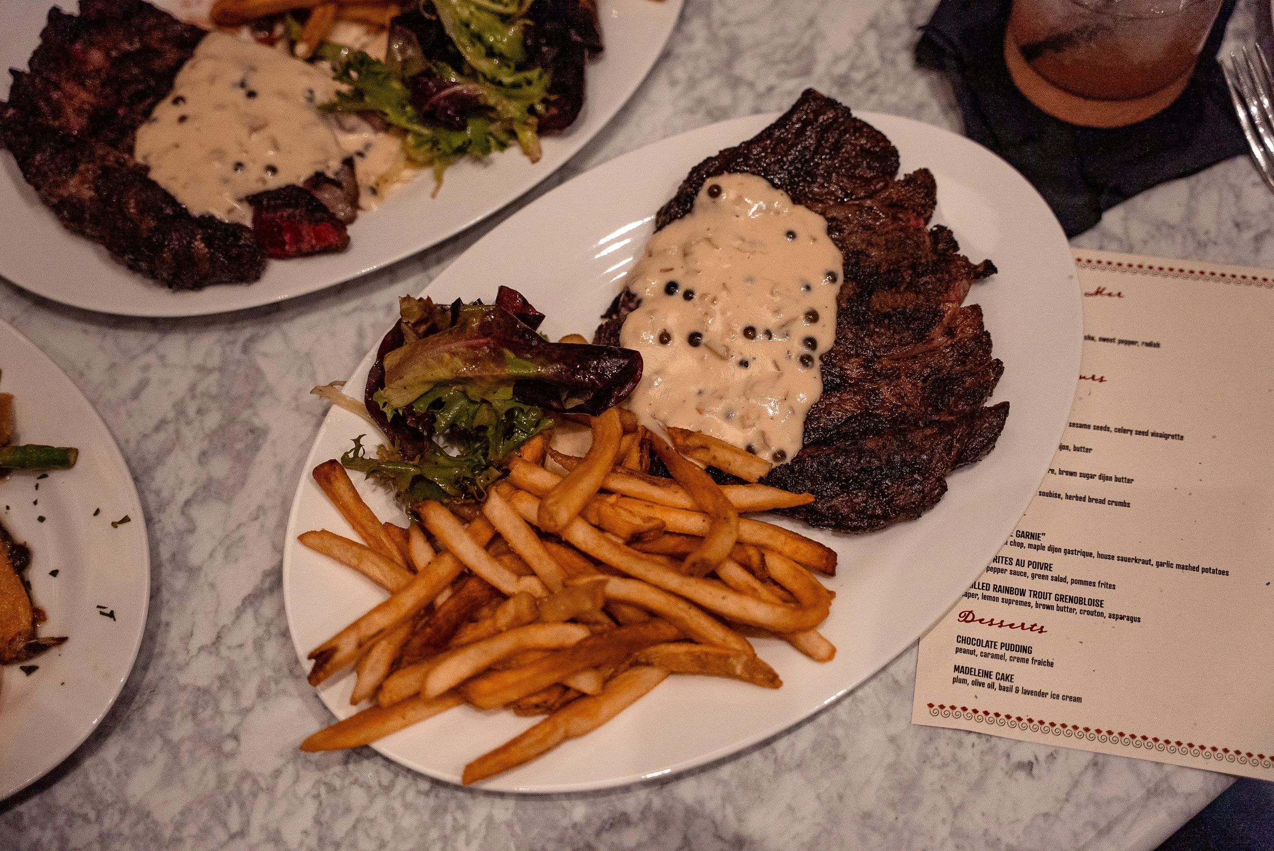Plate of grilled meat topped with creamy mushroom sauce, served with French fries and side salad with mixed greens on a white oval plate.