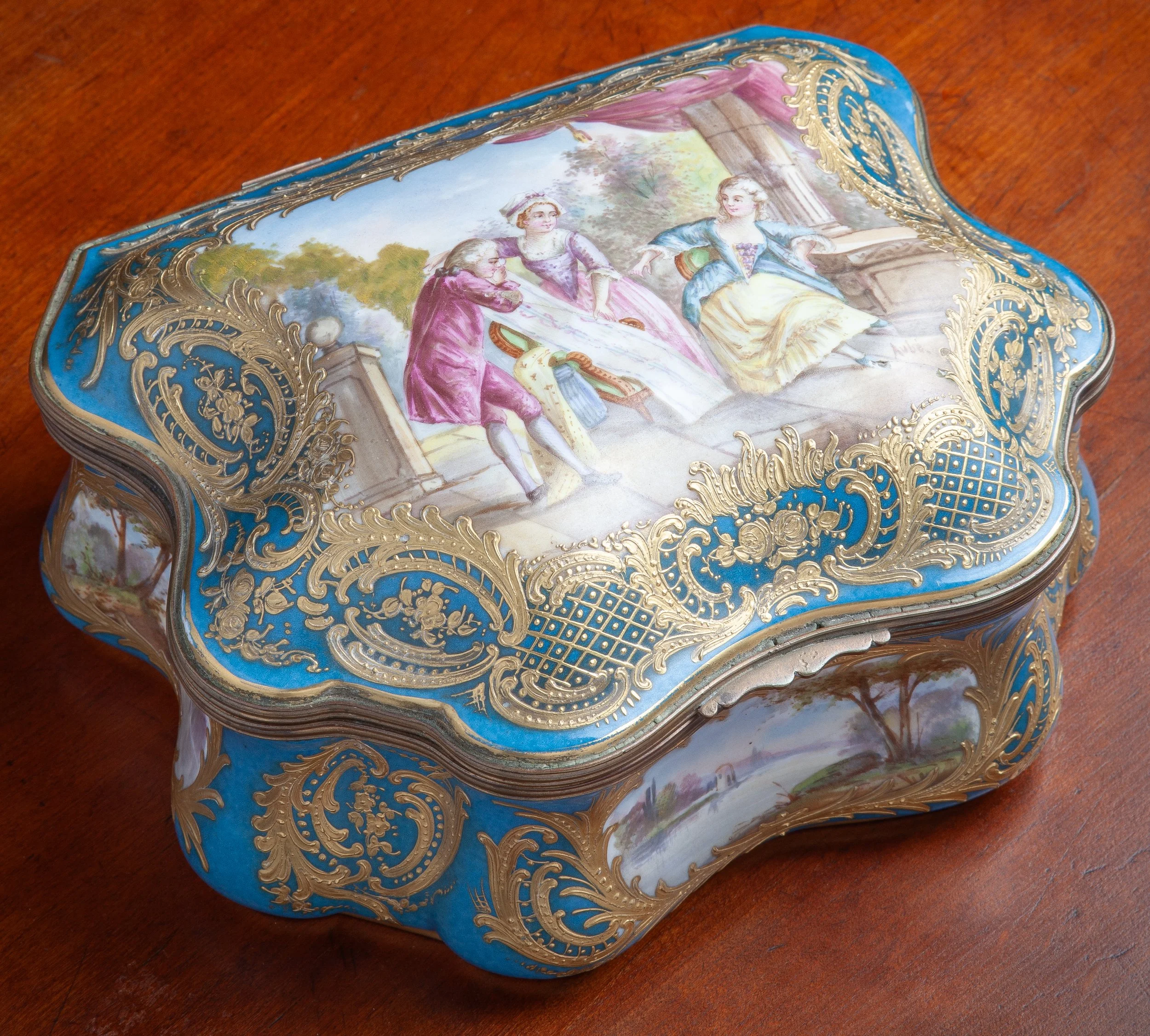 AN ANTIQUE, FRENCH PORCELAIN TRINKET BOX, HAVING A TURQUOISE BLUE GROUND WITH EXTENSIVE GOLD GILDED DECORATIONS. THE HAND-PAINTED LID FEATURES A LADY AND HER MAID BEING GREETED BY A GENTLEMAN. THE SIDES FEATURE LANDSCAPE VIGNETTES. 