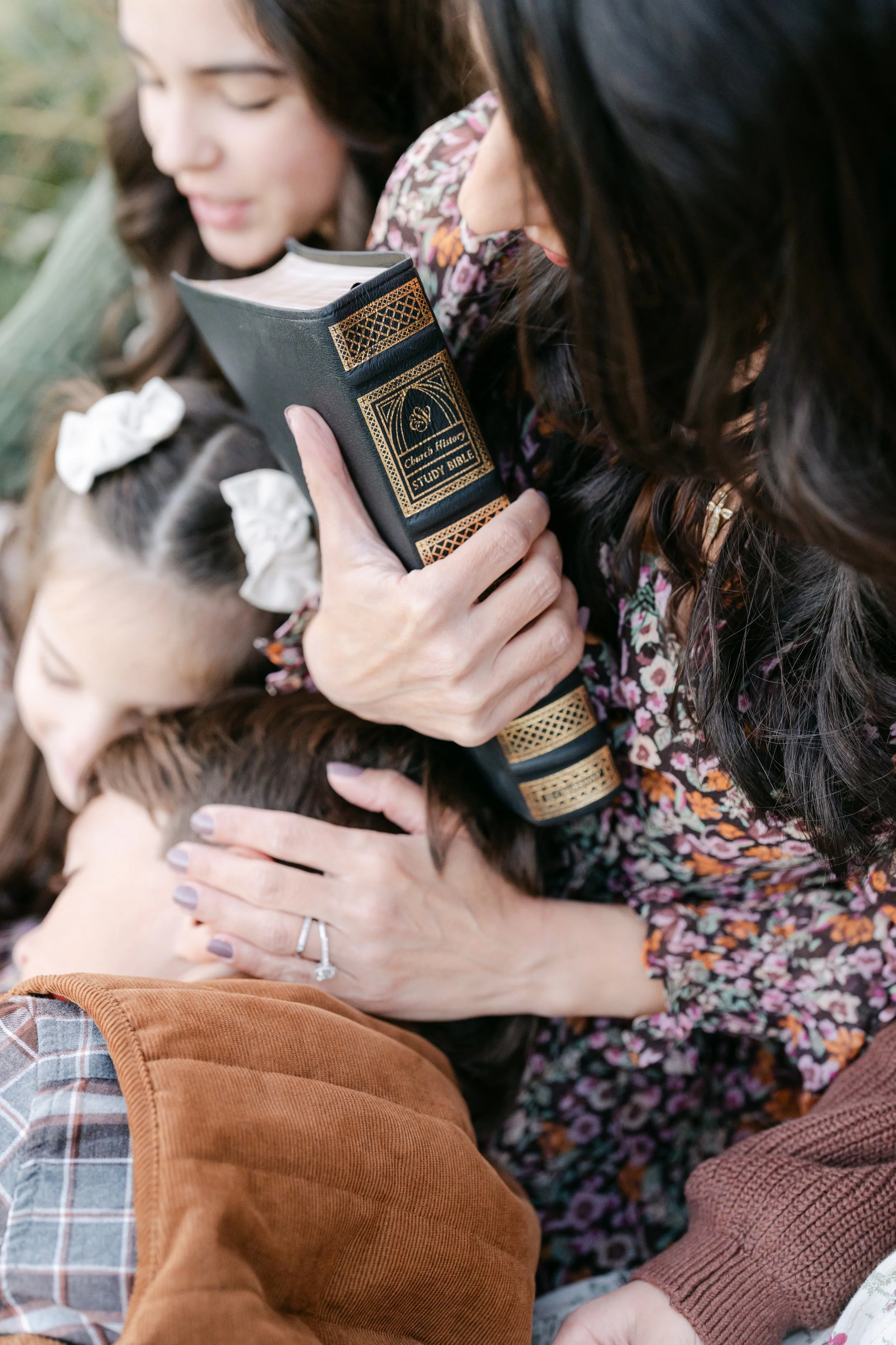 mother reading Bible with children outdoors
