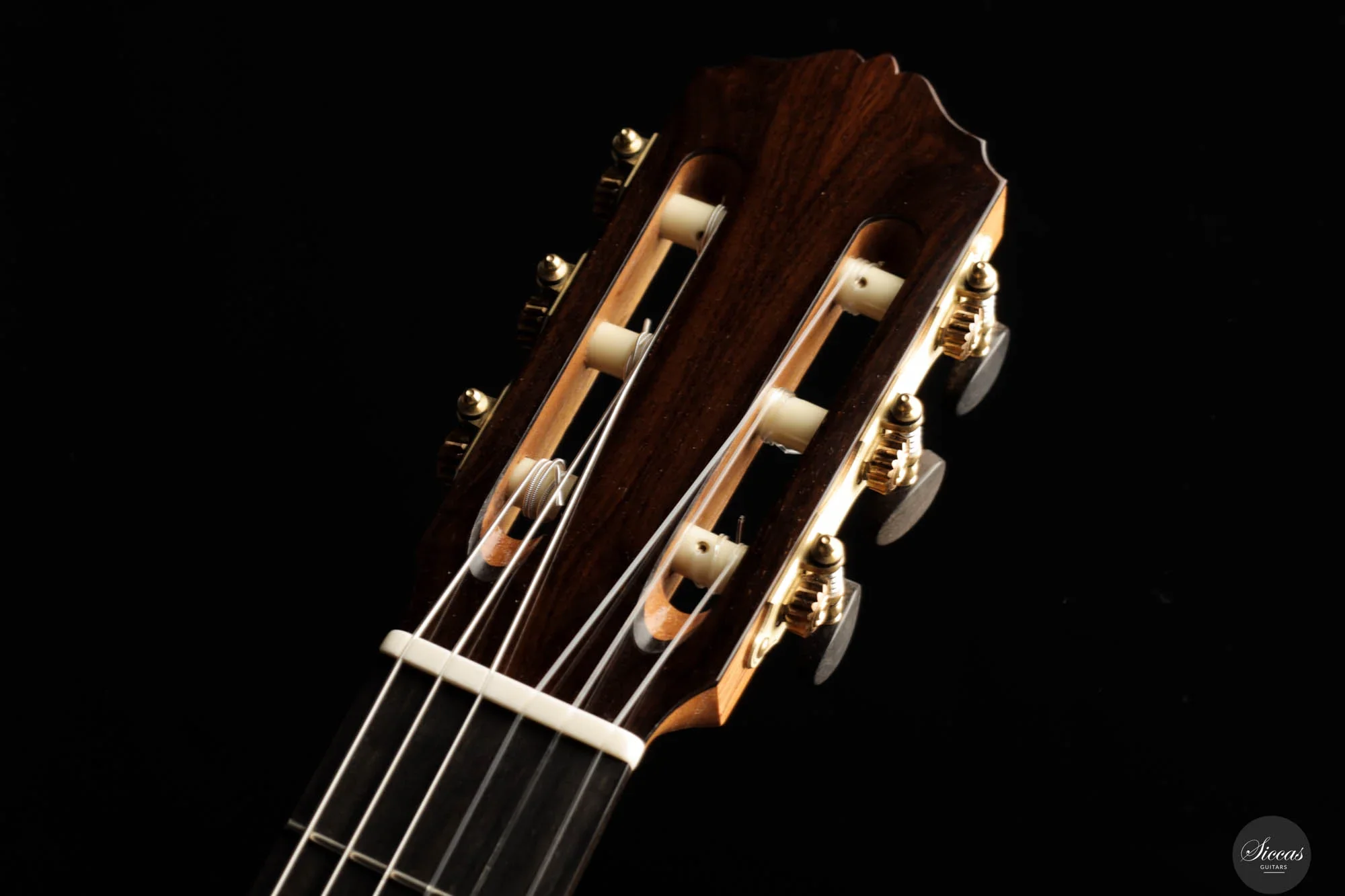Close-up of a classical guitar headstock with tuning pegs, strings, and wooden finish against a black background.