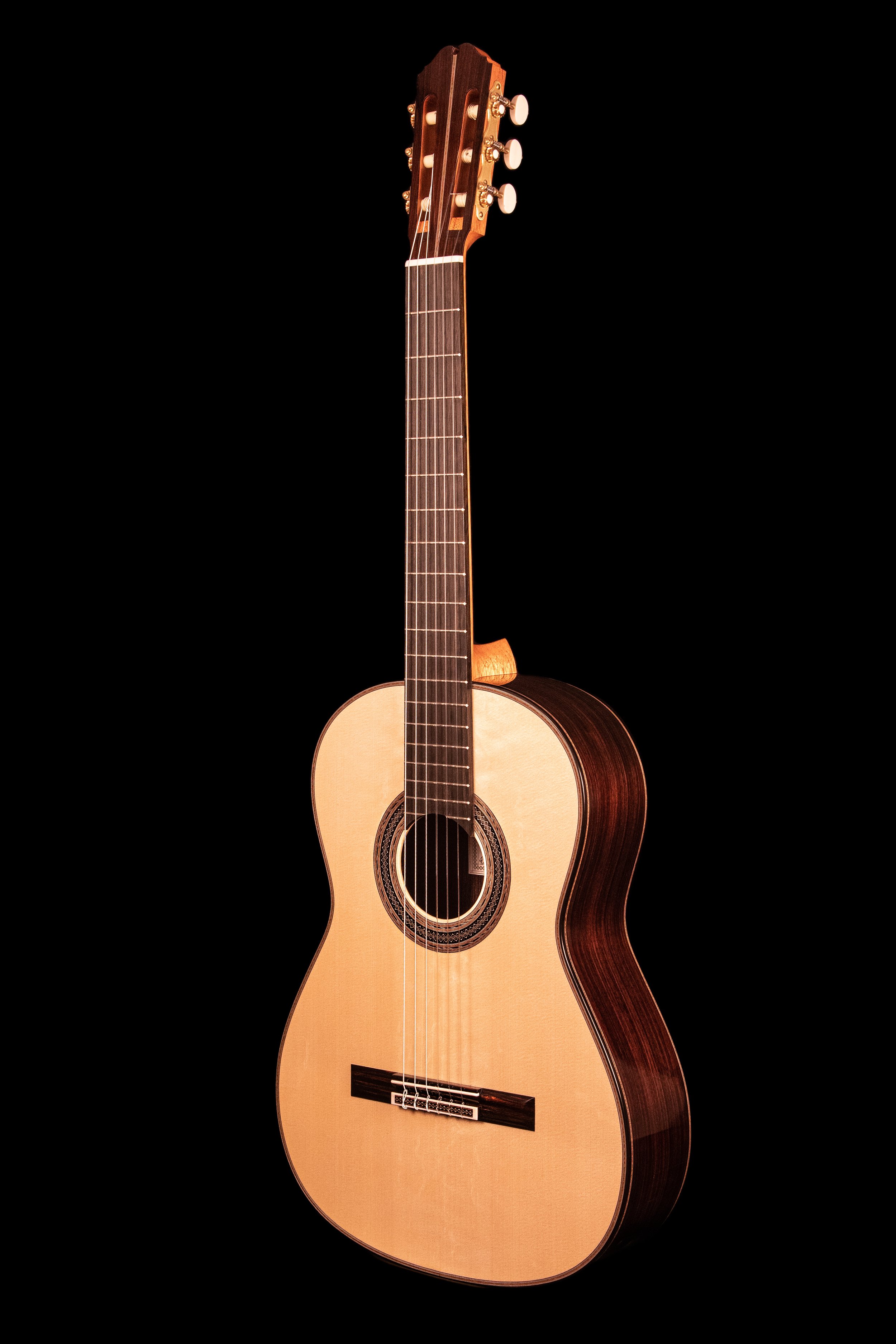 An acoustic guitar with a wooden body and dark fretboard against a black background.
