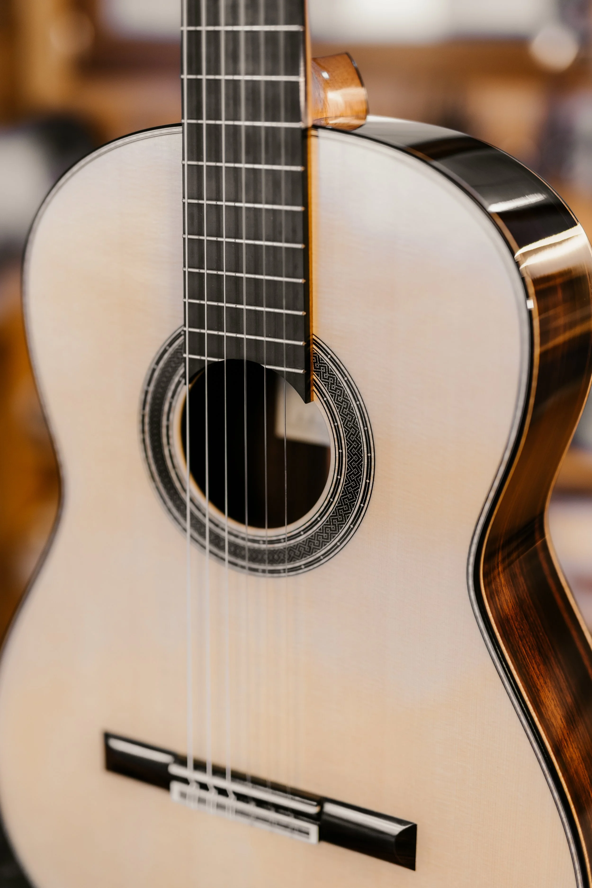 Close-up of an acoustic guitar with a light-colored top, dark fretboard, and decorative rosette around the sound hole.